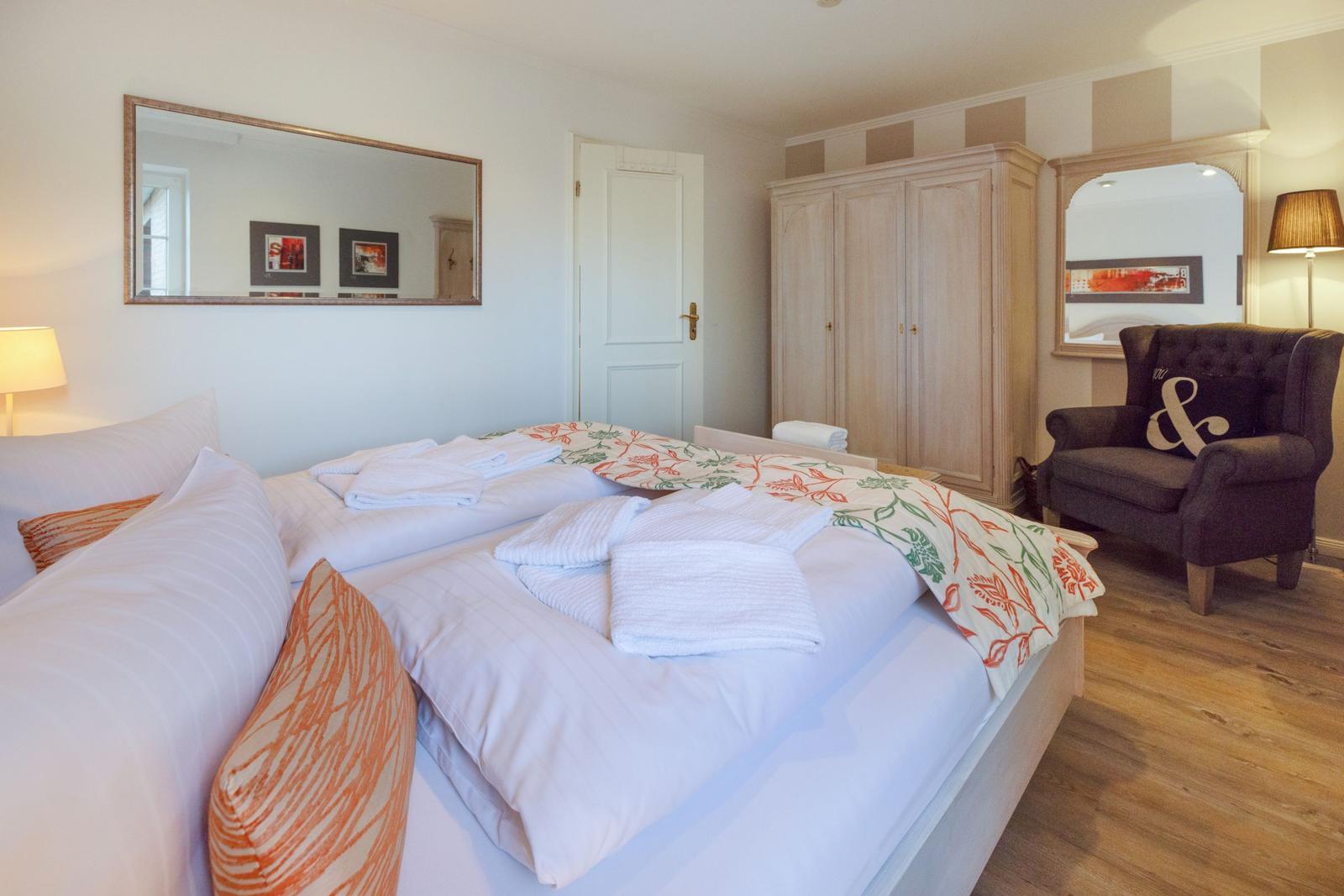 A bedroom with a double bed, wardrobe, and armchair.