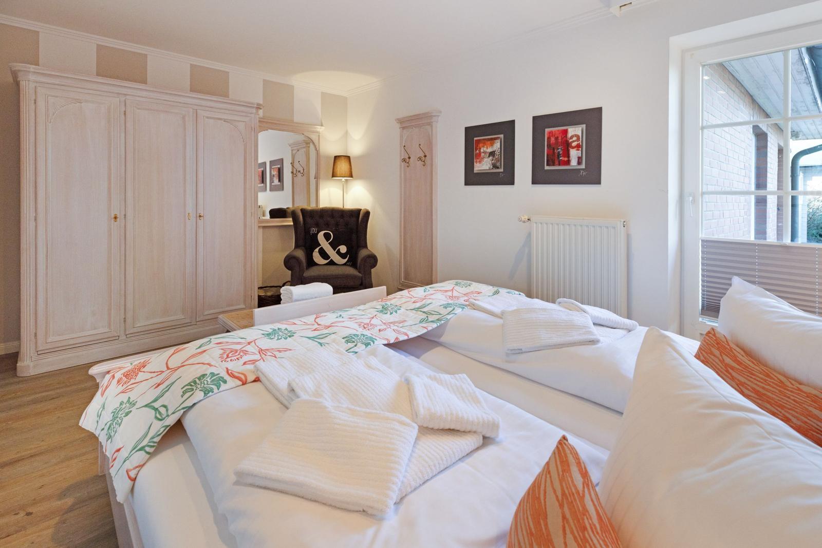 Room with double bed, wardrobe, and armchair. Window with view of outdoor area.