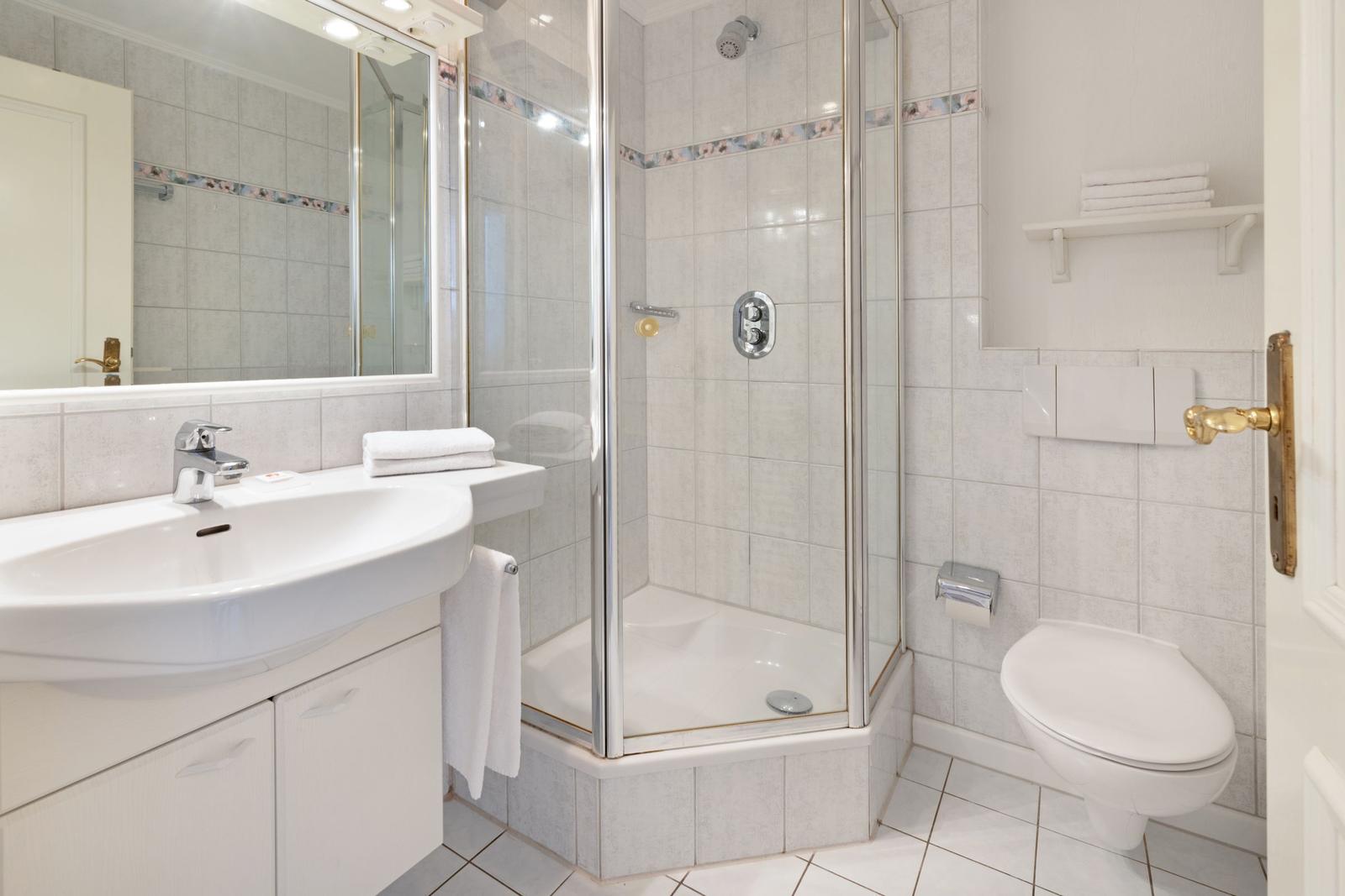 Bathroom with shower, sink, and toilet. Tiles and white sanitary fixtures.