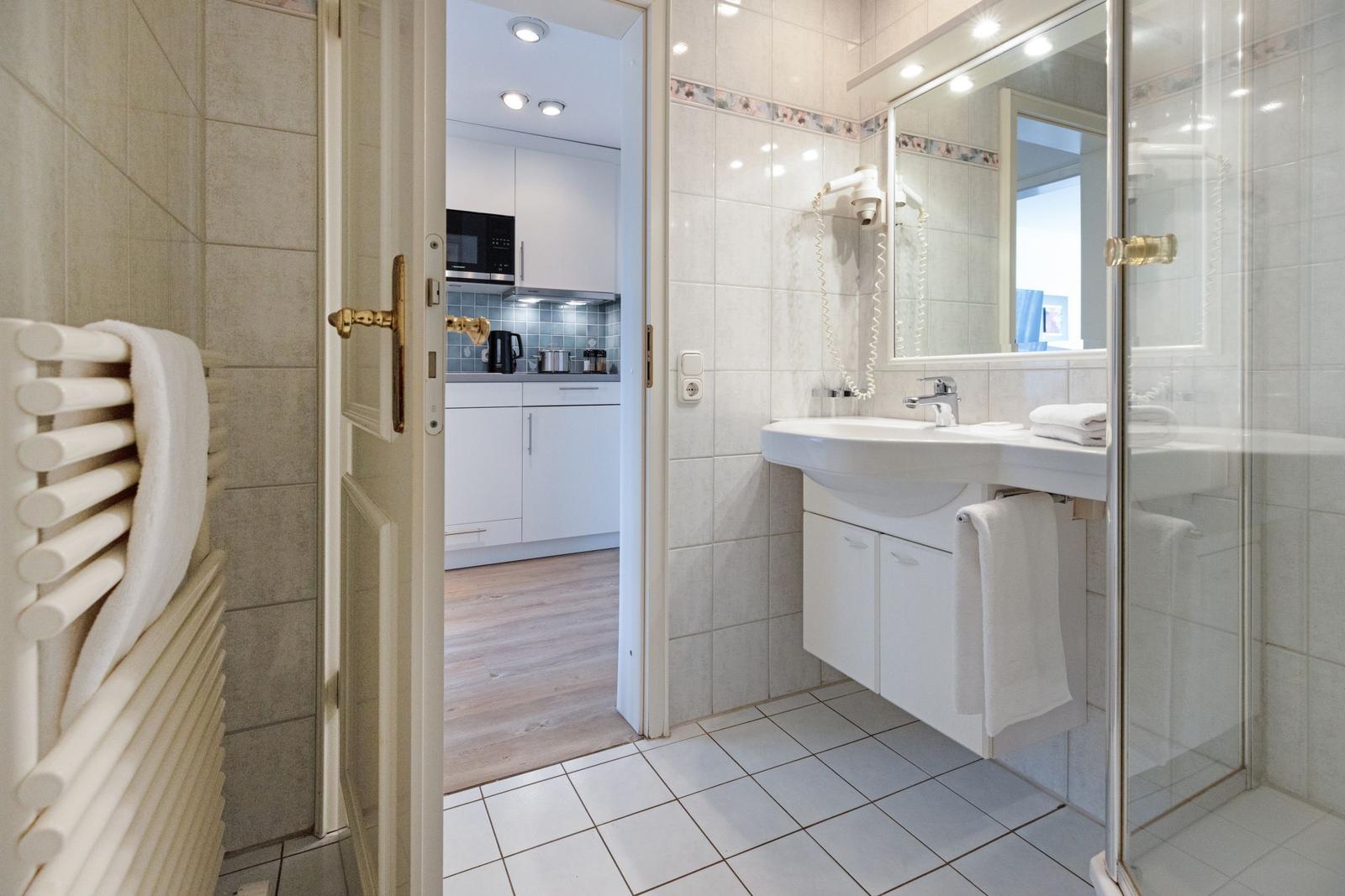 Bathroom with shower, sink, and view into the kitchen.