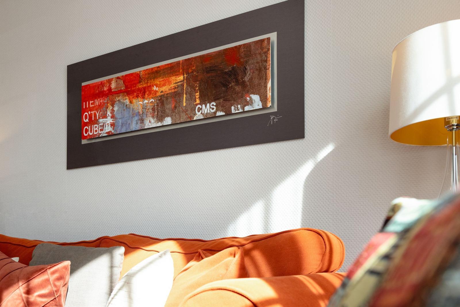 Orange sofa with cushions under an abstract wall picture and a floor lamp.