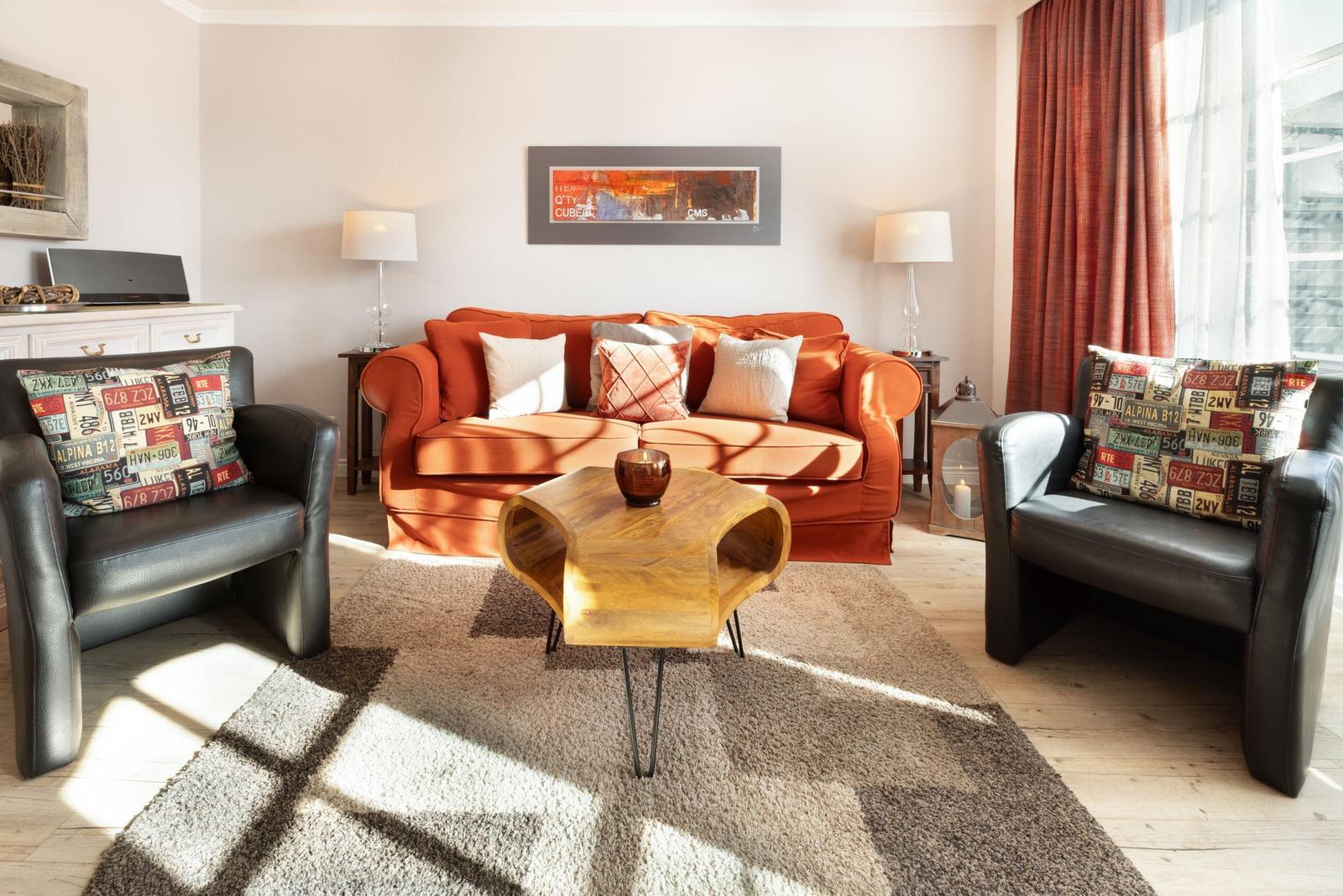 A living room with an orange sofa, two black chairs, and a wooden table.