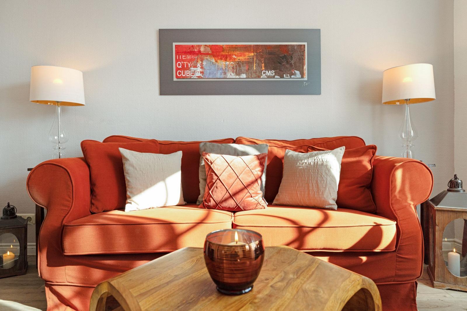 A red sofa with cushions, table, lamps, and wall art.