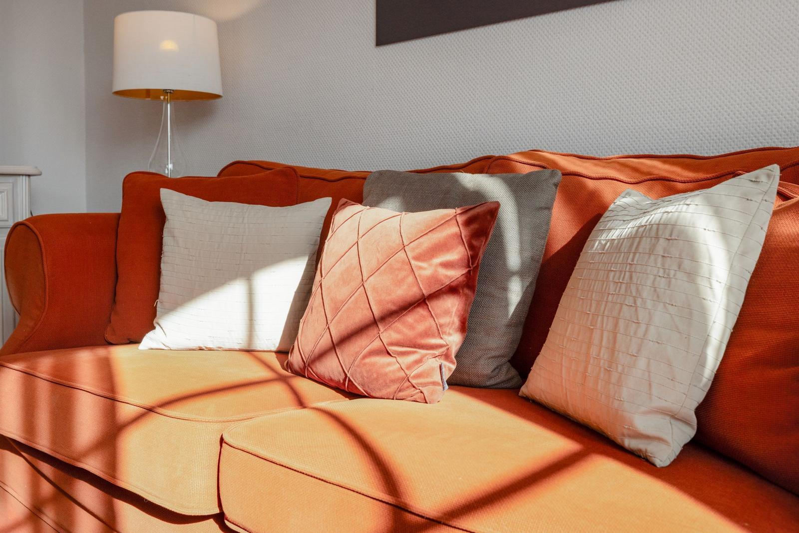 Orange sofa with cushions and floor lamp in a living room.