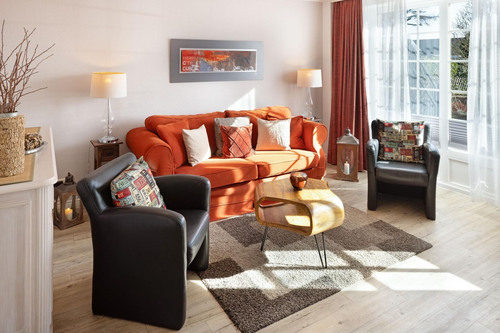 A living room with an orange sofa, two black chairs, and a wooden table.