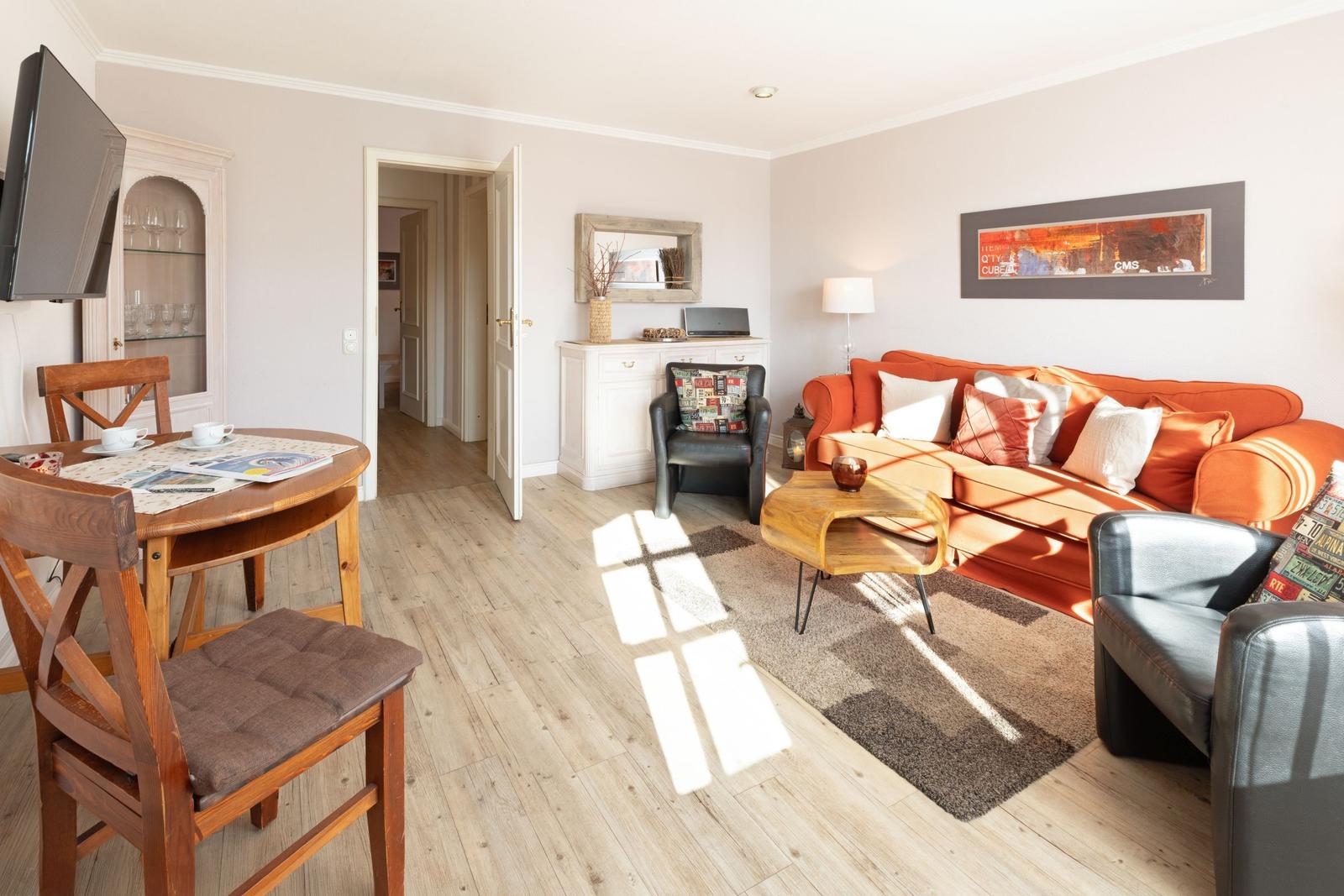 Living and dining area with orange sofa, wooden table, and TV.