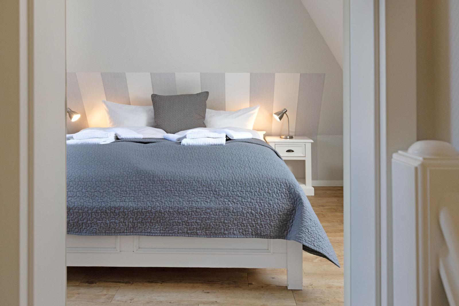 Schlafzimmer mit Bett, Nachttisch und Stehlampe. Holzboden und schräges Dach.
