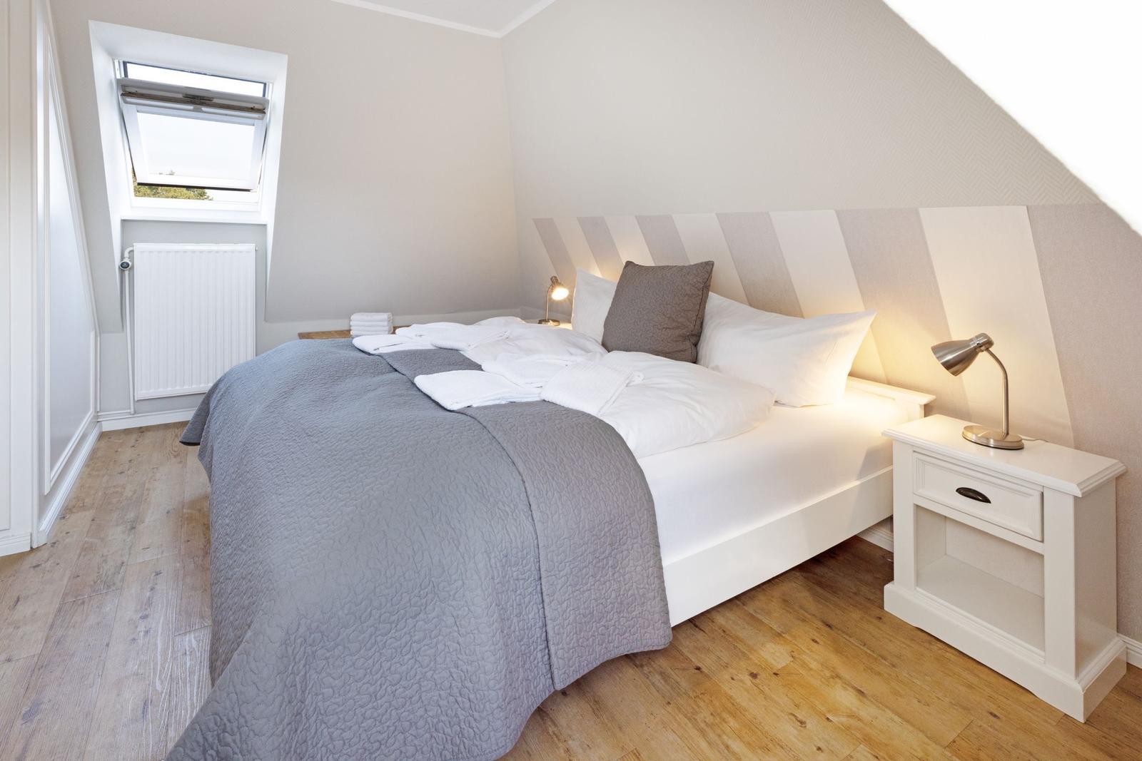 Schlafzimmer mit Dachschrägen, Bett, Nachttisch und Fenster.