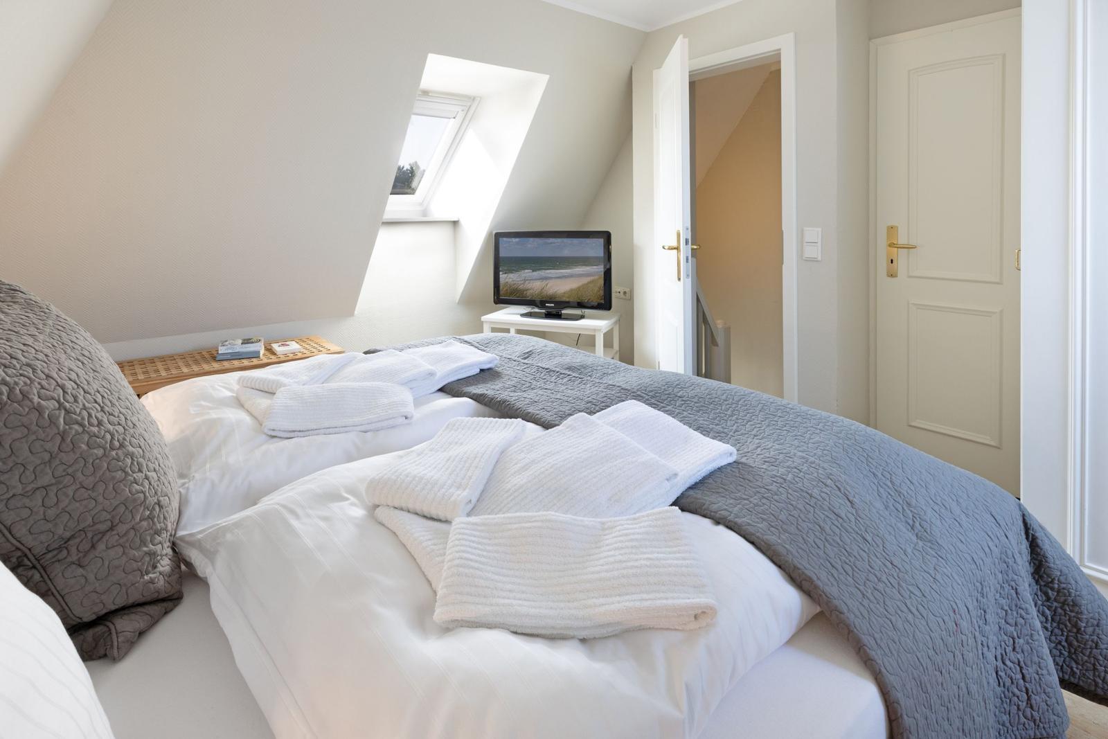Schlafzimmer mit Dachschrägen, Bett mit Handtüchern, TV und Dachfenster.
