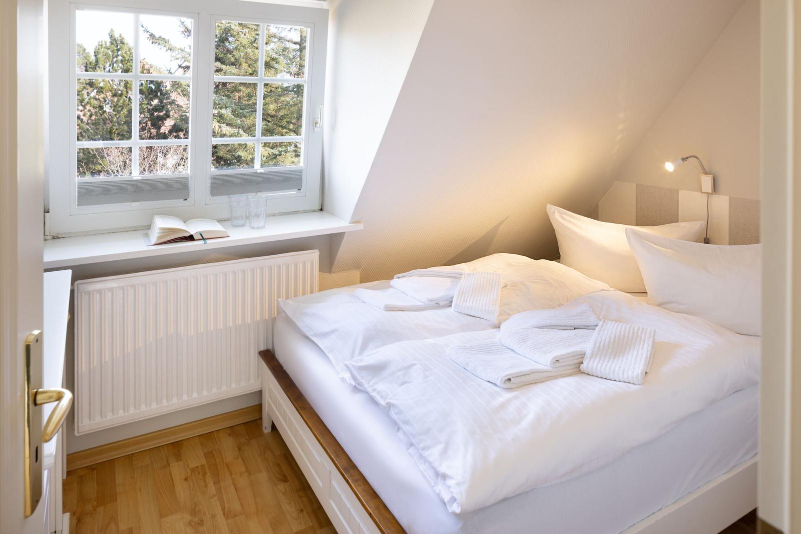 Schlafzimmer mit Dachschräge, Fenster, Bett und Heizkörper.