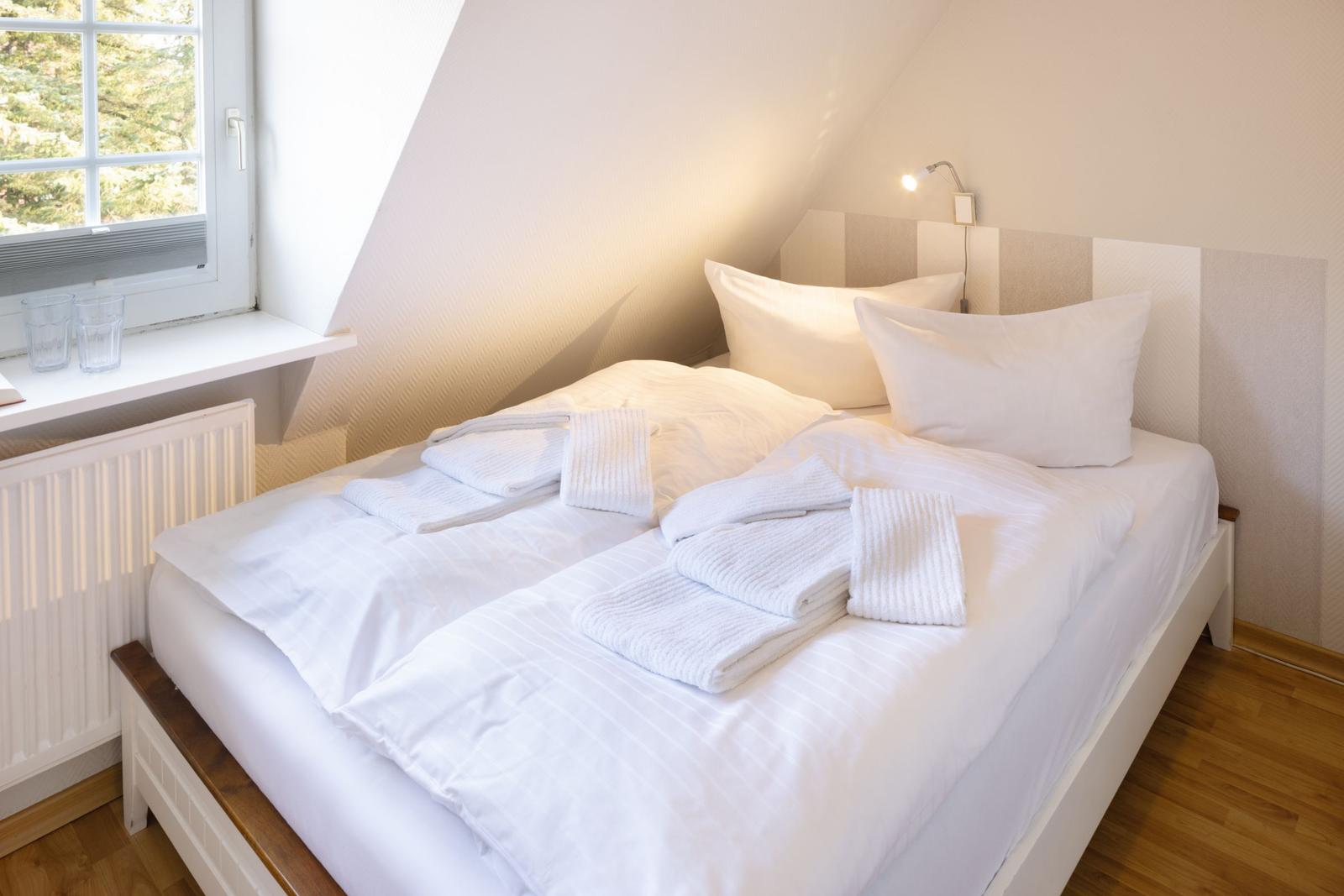 Schlafzimmer mit Doppelbett, Fenster und Stehlampe.