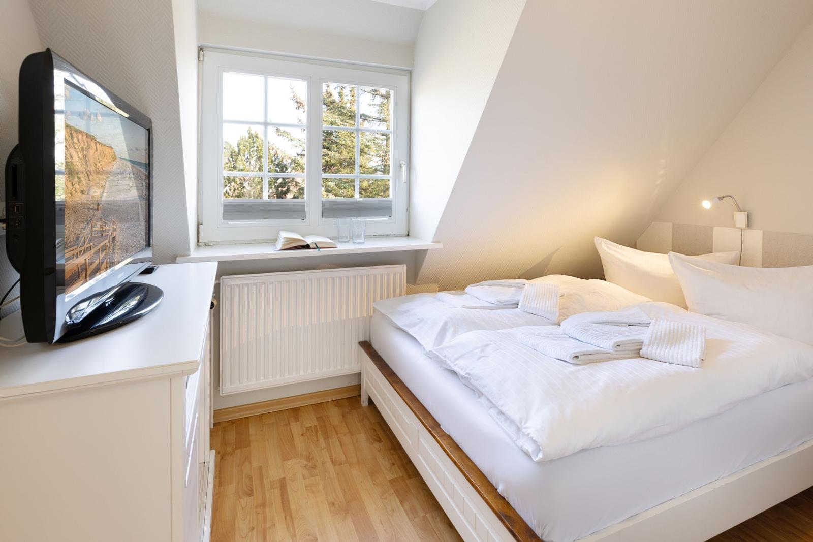 Schlafzimmer mit Dachschräge, Bett, TV und Fenster mit Blick auf Bäume.