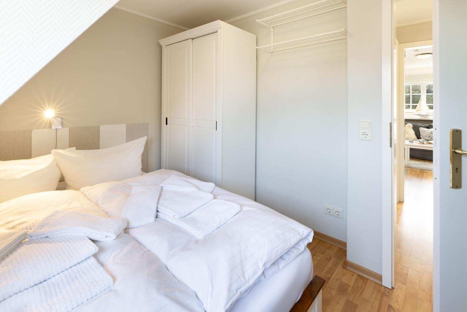 Schlafzimmer mit weißem Bett, Kleiderschrank und Blick in Wohnbereich.