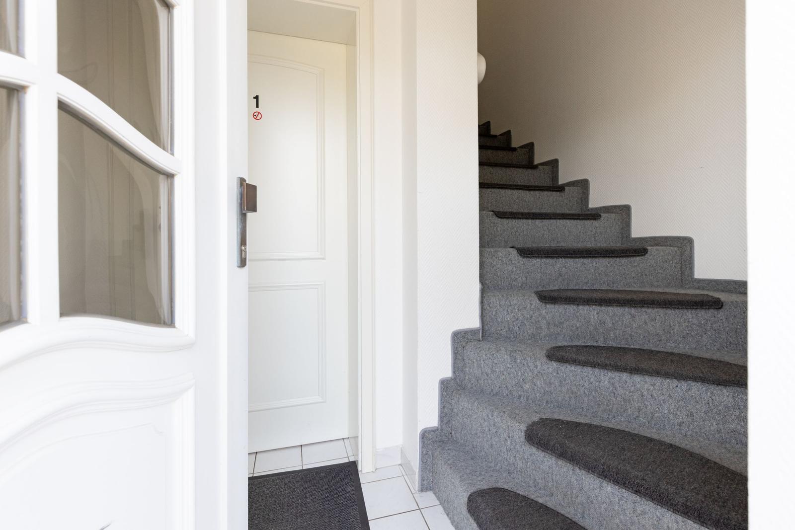 Haus mit weißen Wänden und grauer Treppe mit Teppichstufen.