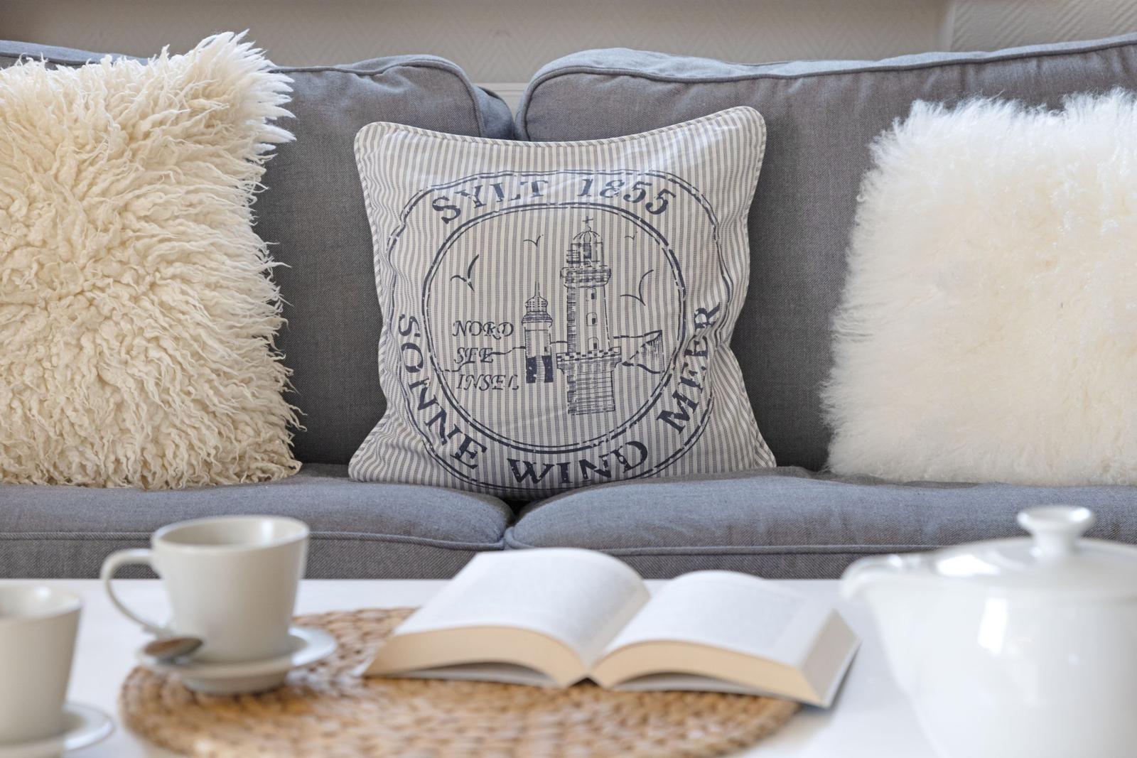 Ein grauer Sofa mit Kissen, darunter ein Tisch mit Tasse, Buch und Teekanne.