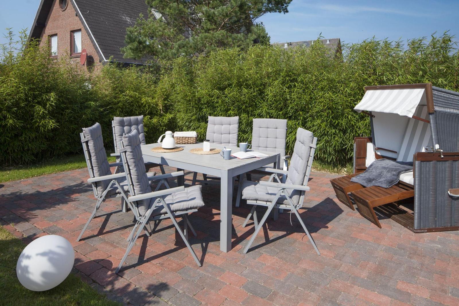 Terrasse mit Gartentisch, sechs Stühlen und Strandkörben. Hintergrund: grüne Hecke und Haus.