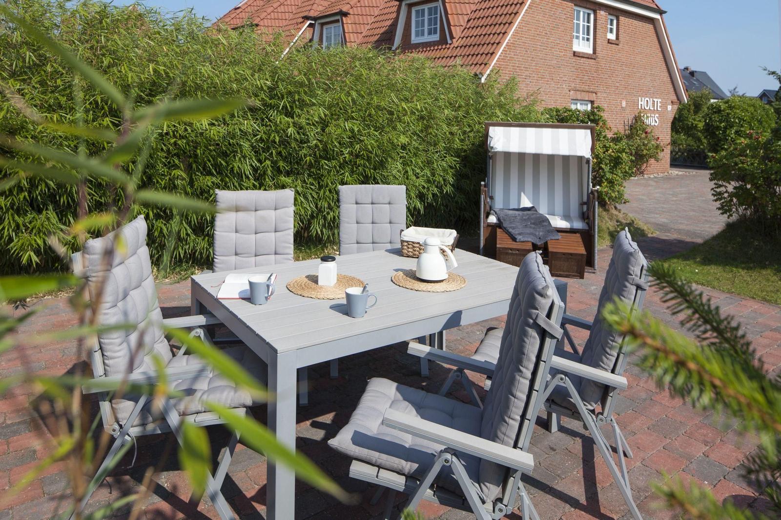 Garten mit Tisch und Stühlen, Liegestuhl und Haus im Hintergrund.