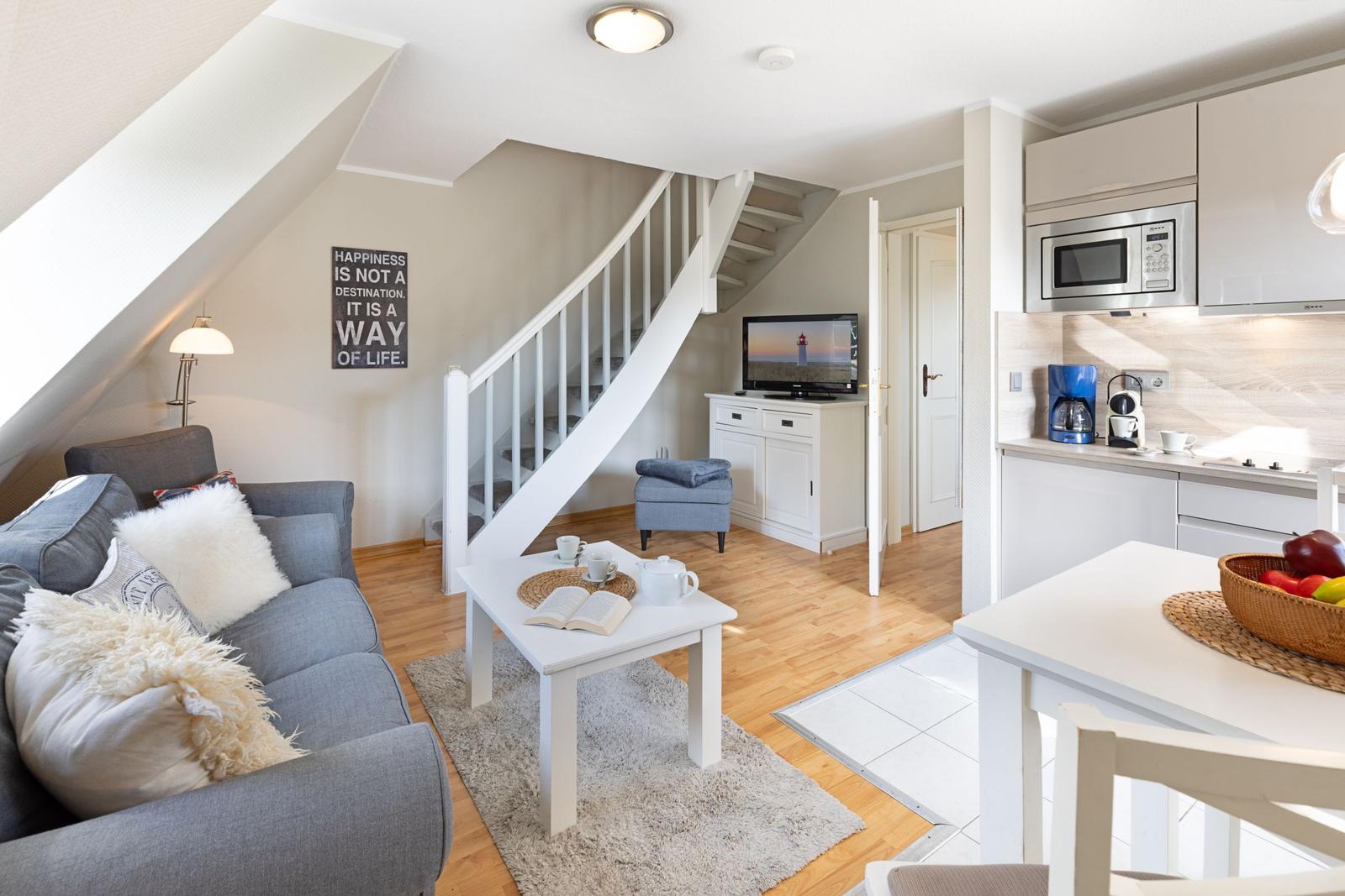 Wohnbereich mit Sofa, Tisch und Treppe. Küche mit Arbeitsplatte und Mikrowelle.