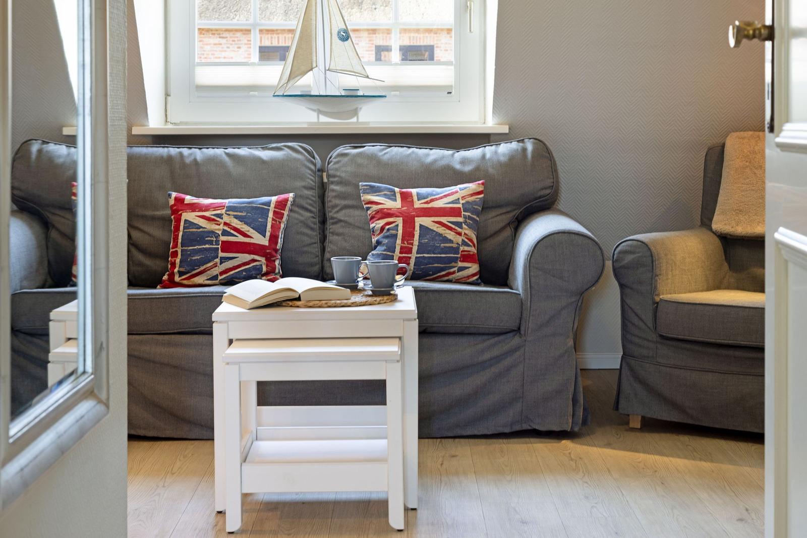 Ein Wohnbereich mit grauem Sofa, zwei Kissen mit britischer Flagge und einem weißen Tisch.