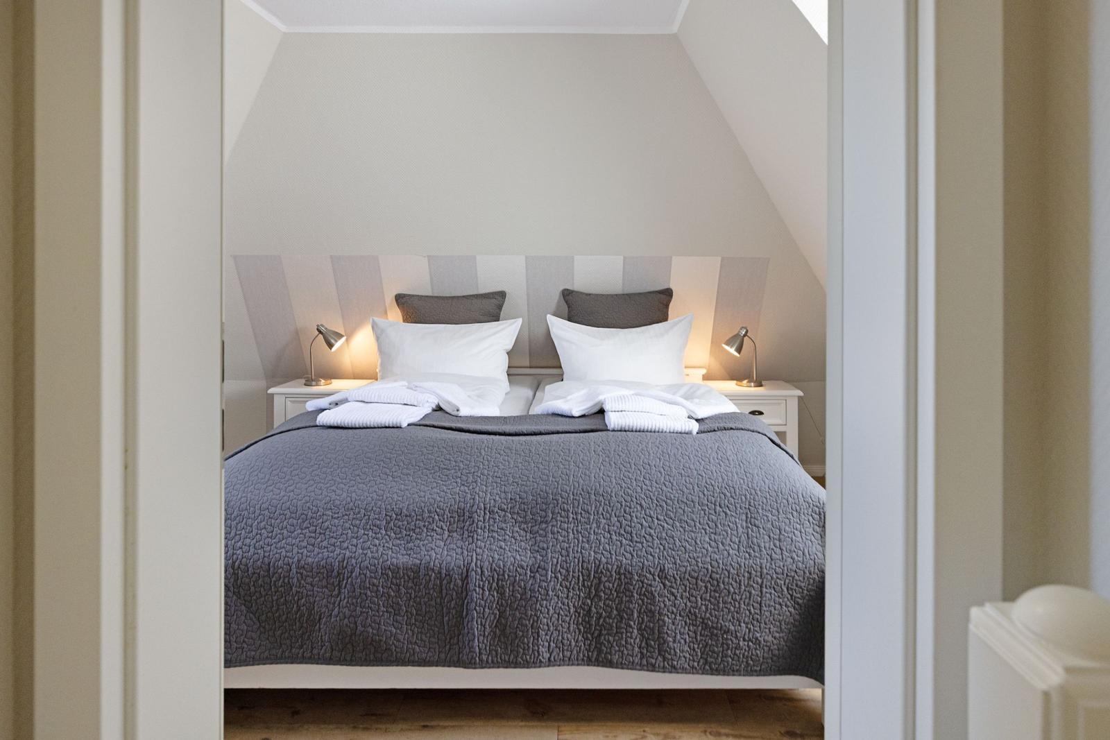 Schlafzimmer mit Doppelbett, zwei Nachttischen und Stehlampen unter schrägem Dach.