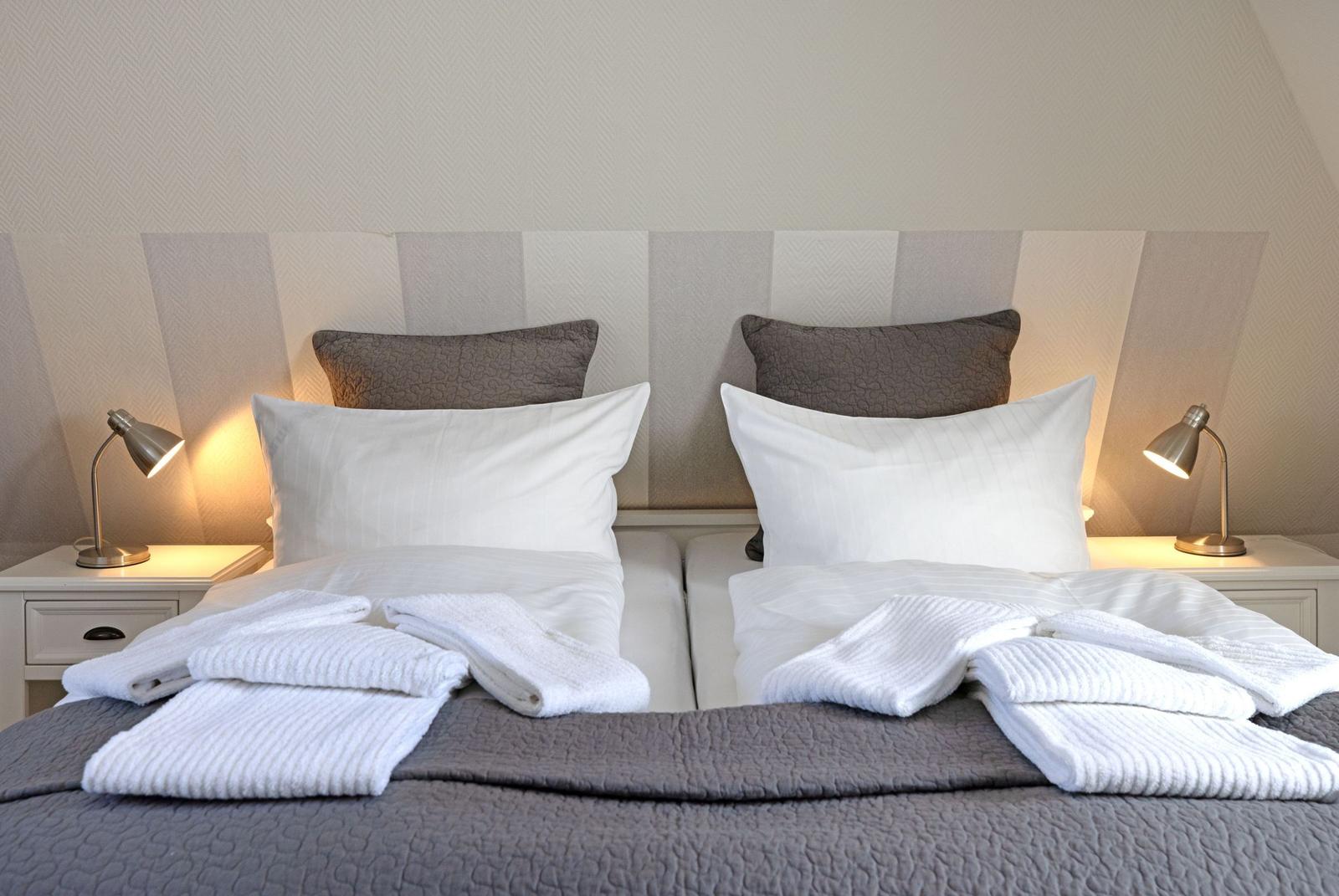 Doppelbett mit weißen Kissen und Handtüchern, zwei Nachttische mit Lampen.
