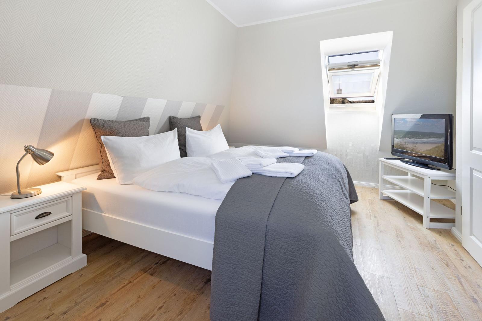 Schlafzimmer mit Bett, Nachttisch, Fernseher und Dachfenster.