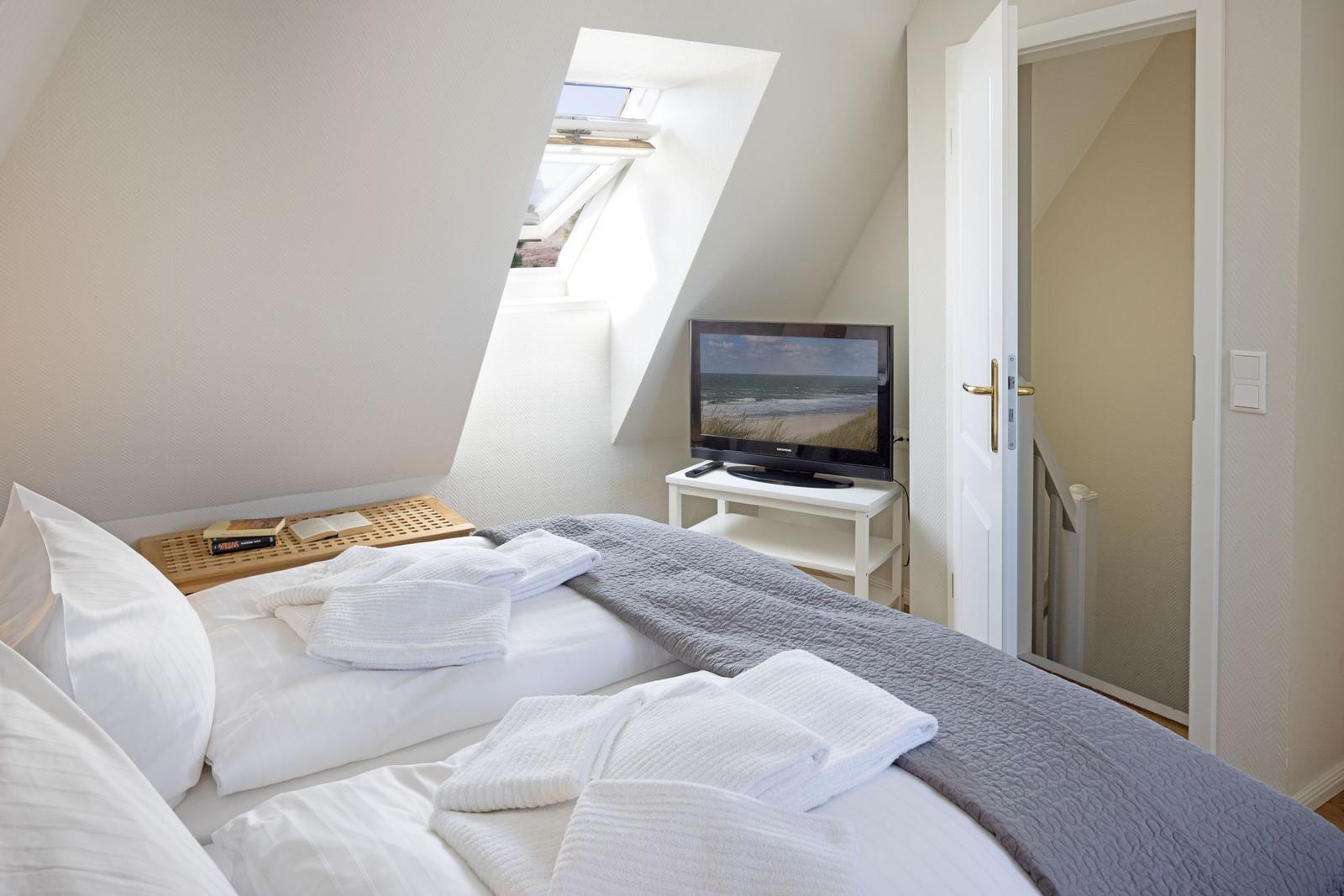 Schlafzimmer mit Dachfenster, Bett, Fernseher und Tür.