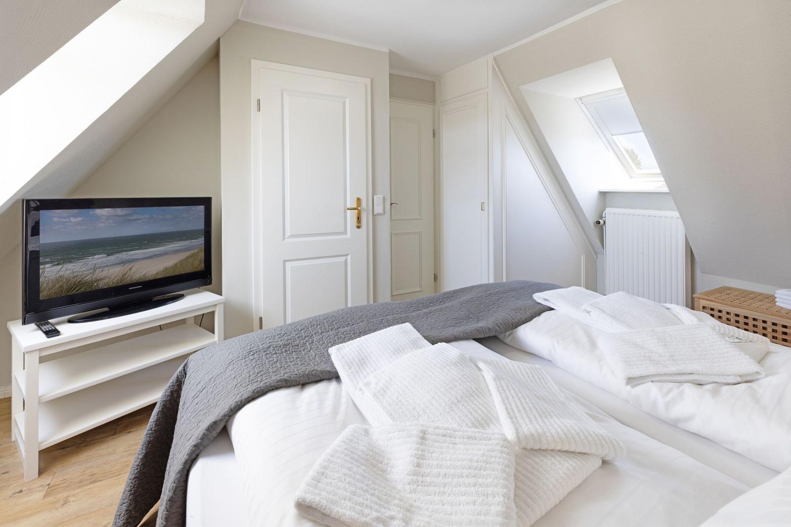 Schlafzimmer mit Dachschräge, Bett, Fernseher und Schrank.