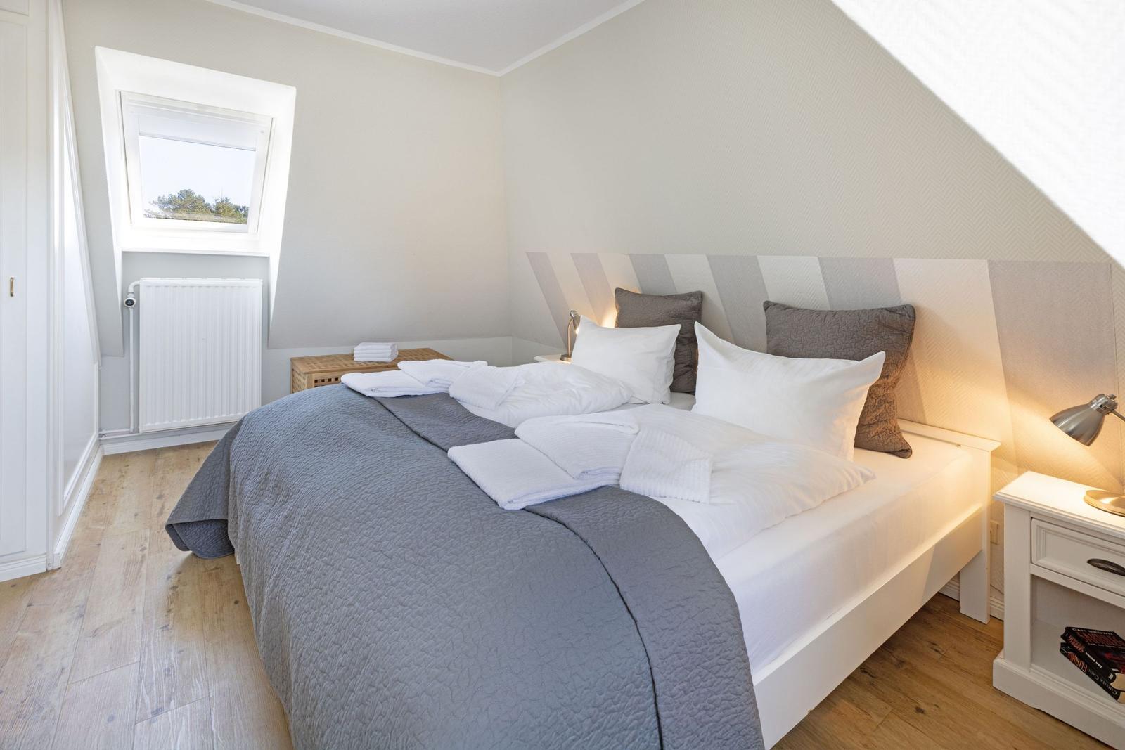 Schlafzimmer mit Dachschräge, Bett, Nachttisch und Fenster
