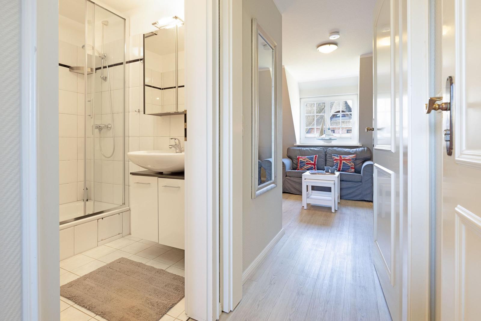 Badezimmer mit Dusche und Waschbecken. Wohnzimmer mit Sofa und Fenster.