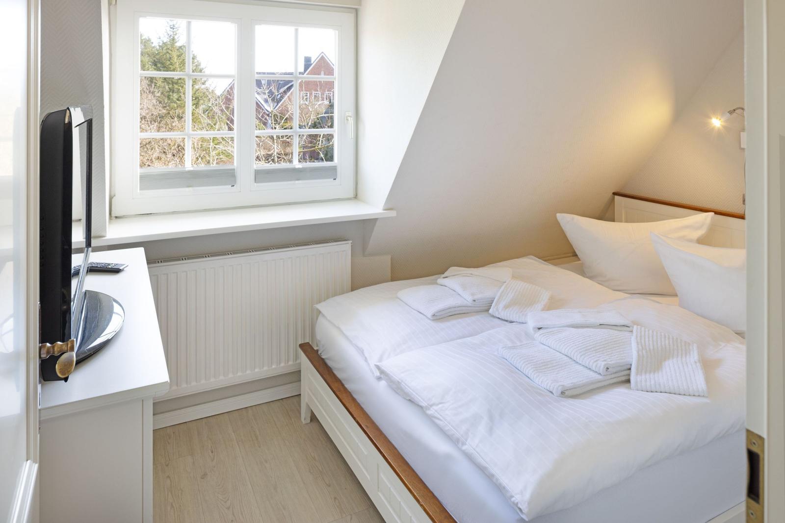 Schlafzimmer mit Dachschräge, Bett mit weißen Bettwäsche und Fernseher an Wand.