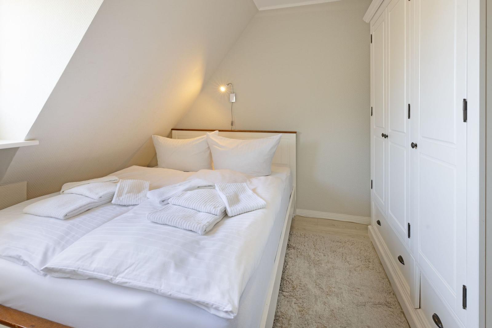 Schlafzimmer mit Dachschräge, weißem Bett und Kleiderschrank.