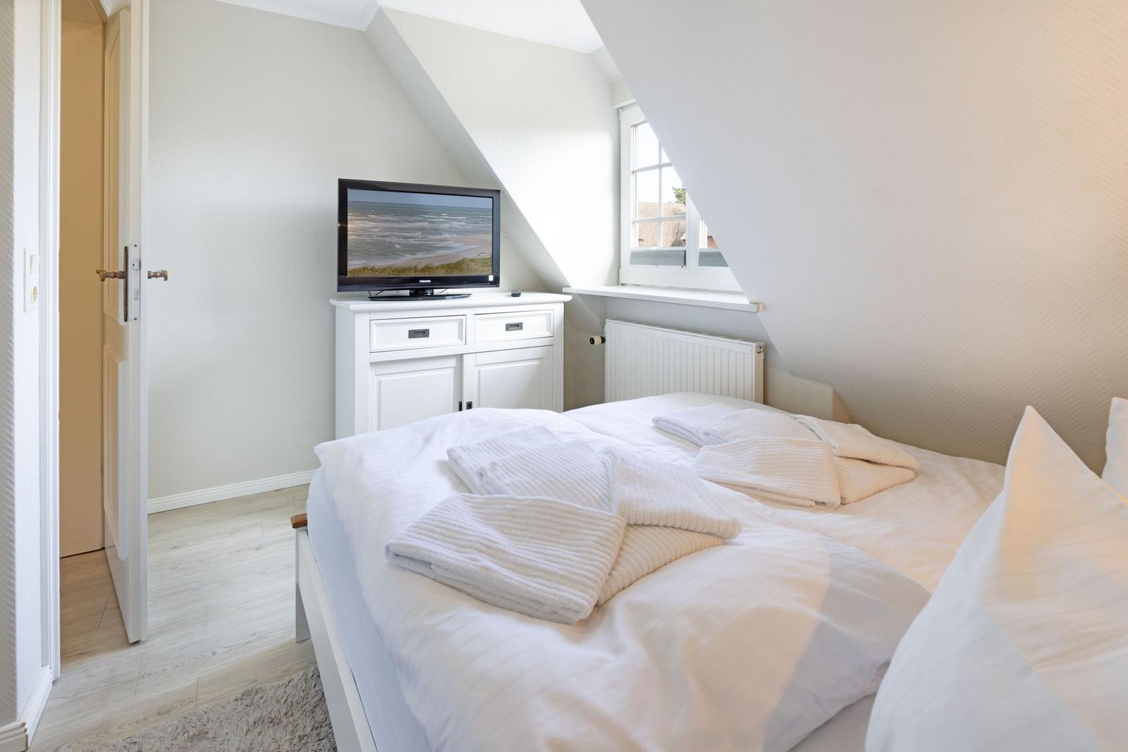 Schlafzimmer mit Dachschräge, Bett, Fernseher und Fenster.