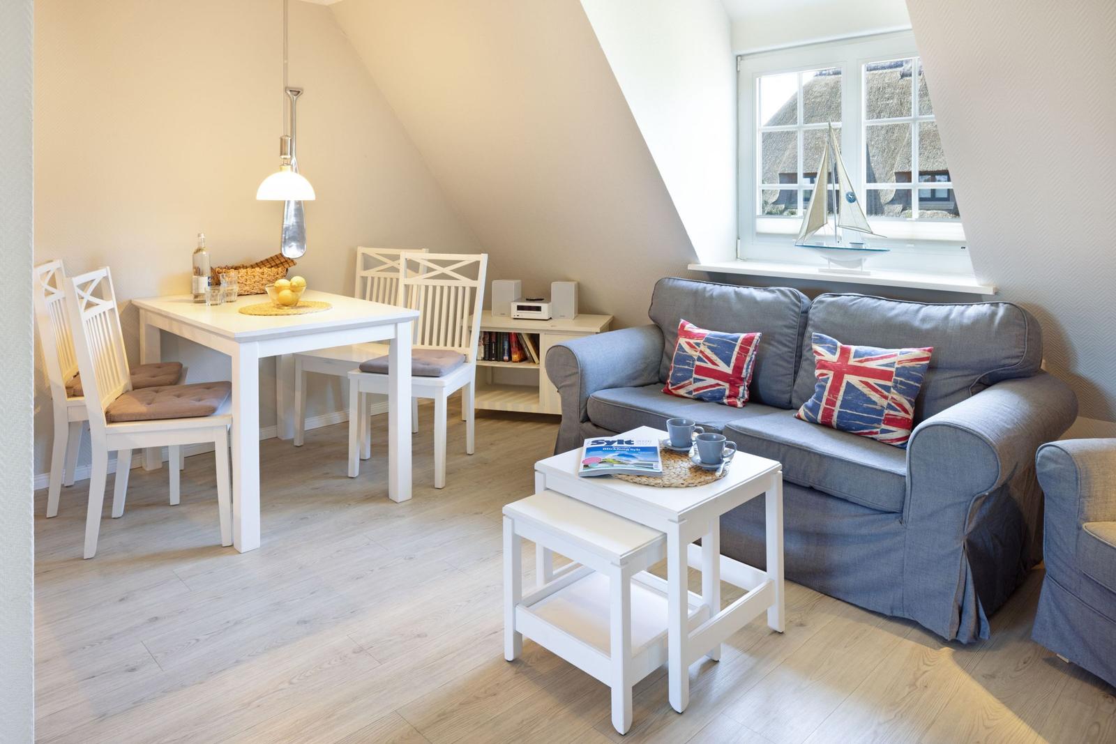 Wohn- und Essbereich mit Sofa, Tisch und Stühlen. Fenster zeigt Dachhäuser.