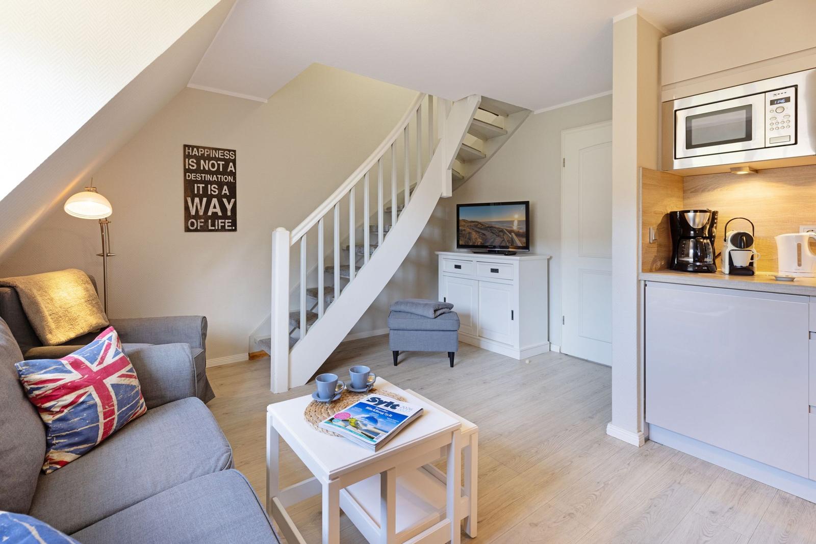 Wohnbereich mit Sofa, Treppe und Küchenzeile. Wandbild und Fernseher sichtbar.