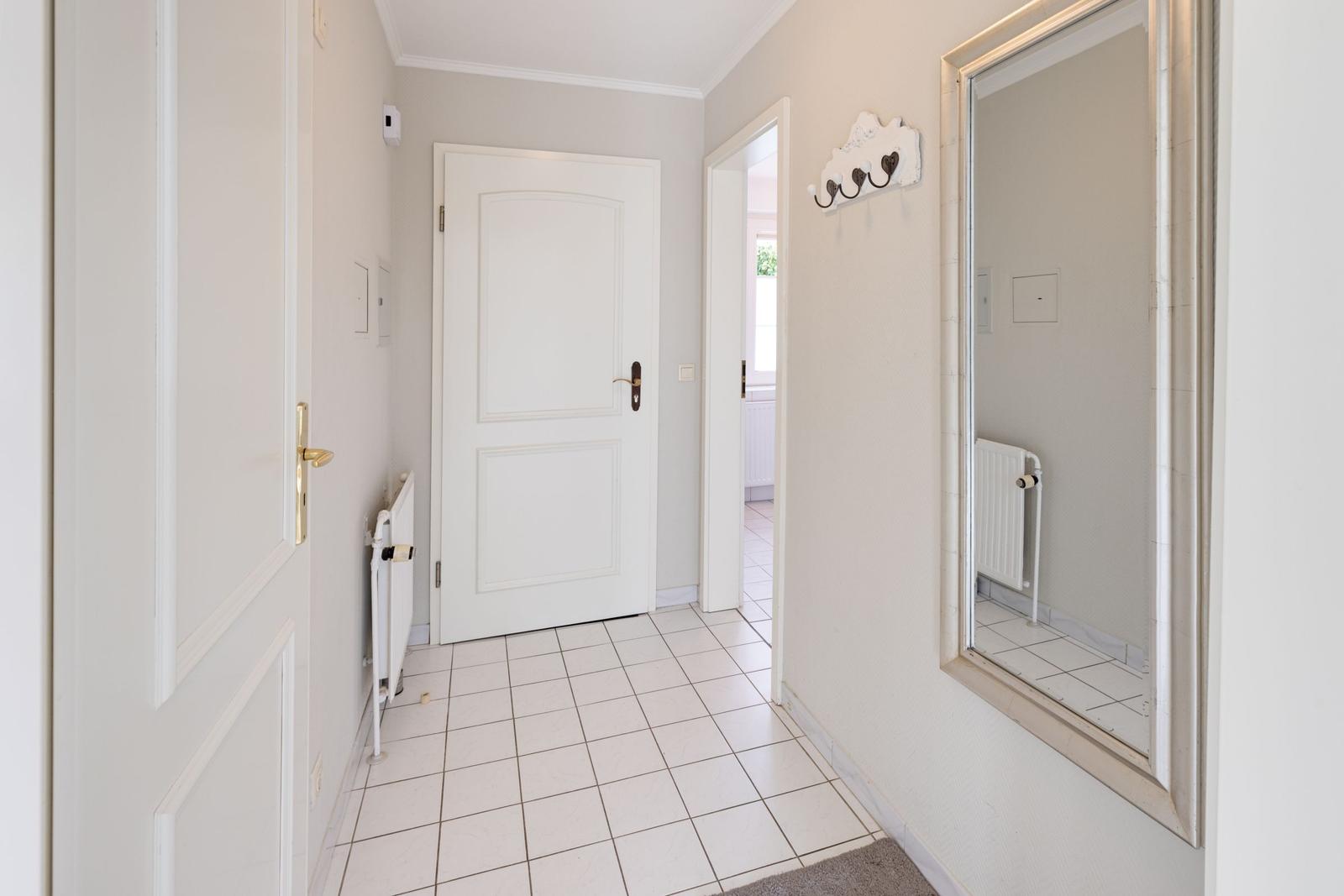 Hallway with white doors, tiled floor, and mirror on the wall.