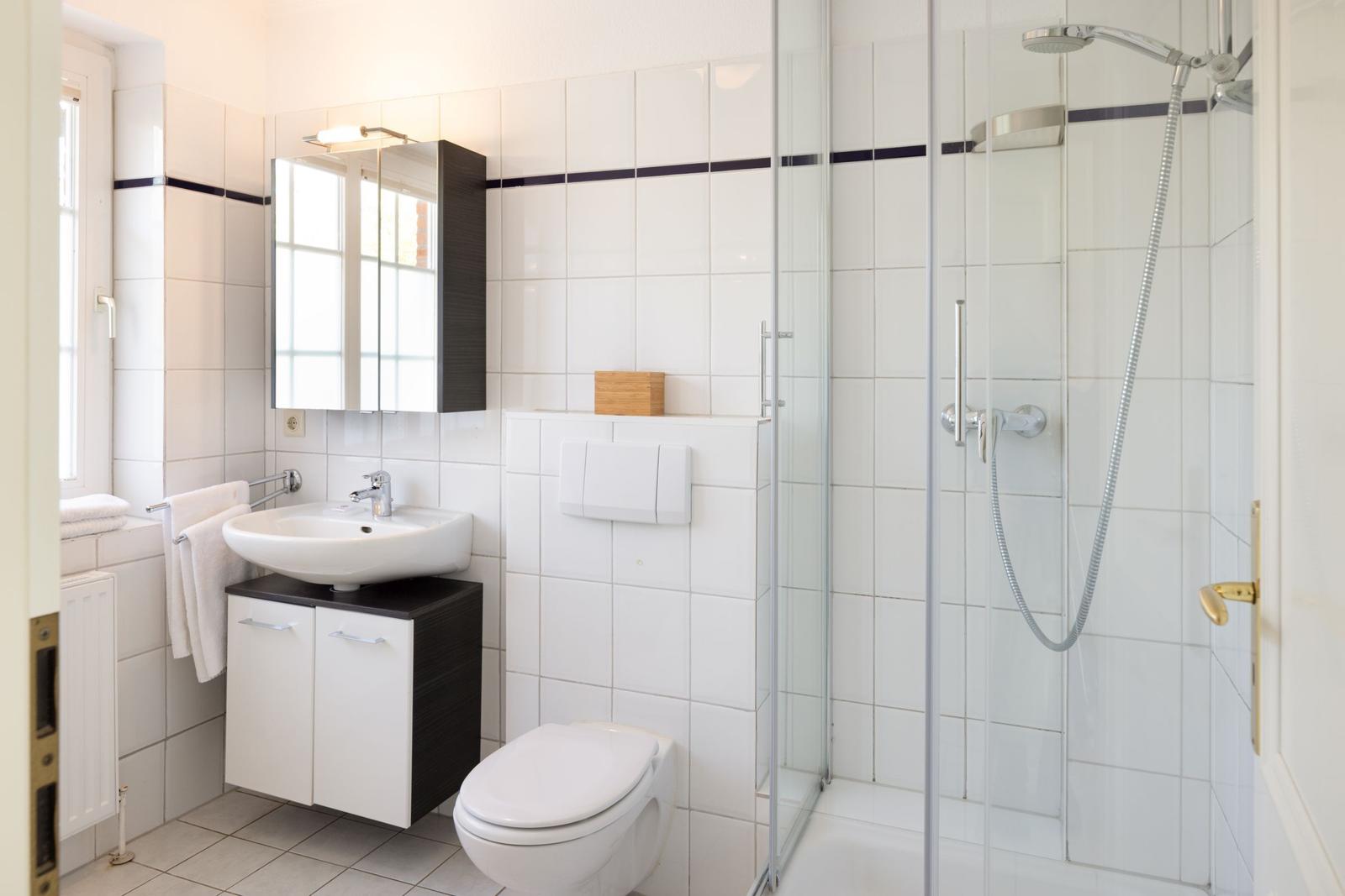 Bathroom with shower, sink, and toilet. White tiles and dark cabinet.