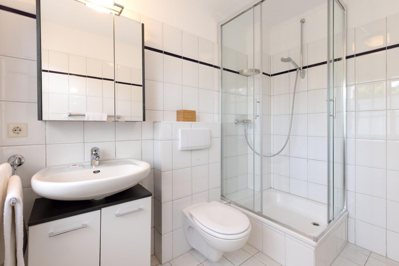 Bathroom with shower, sink and toilet. White tiles and mirror cabinet.
