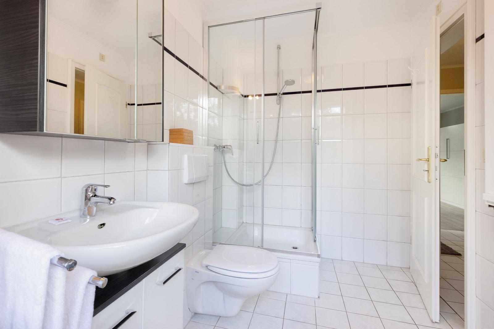 Bathroom with shower, sink, and toilet. White tiles and mirror cabinet.
