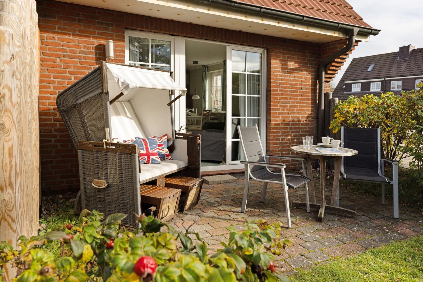 Terrace with lounge chair, table and chairs in front of a house with sliding door.