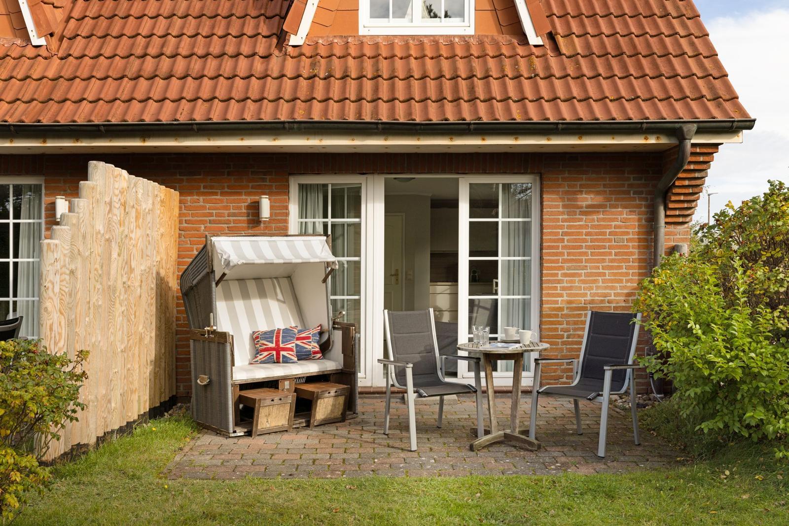 Terrace with lounge, table, and two chairs in front of a house with red roof.