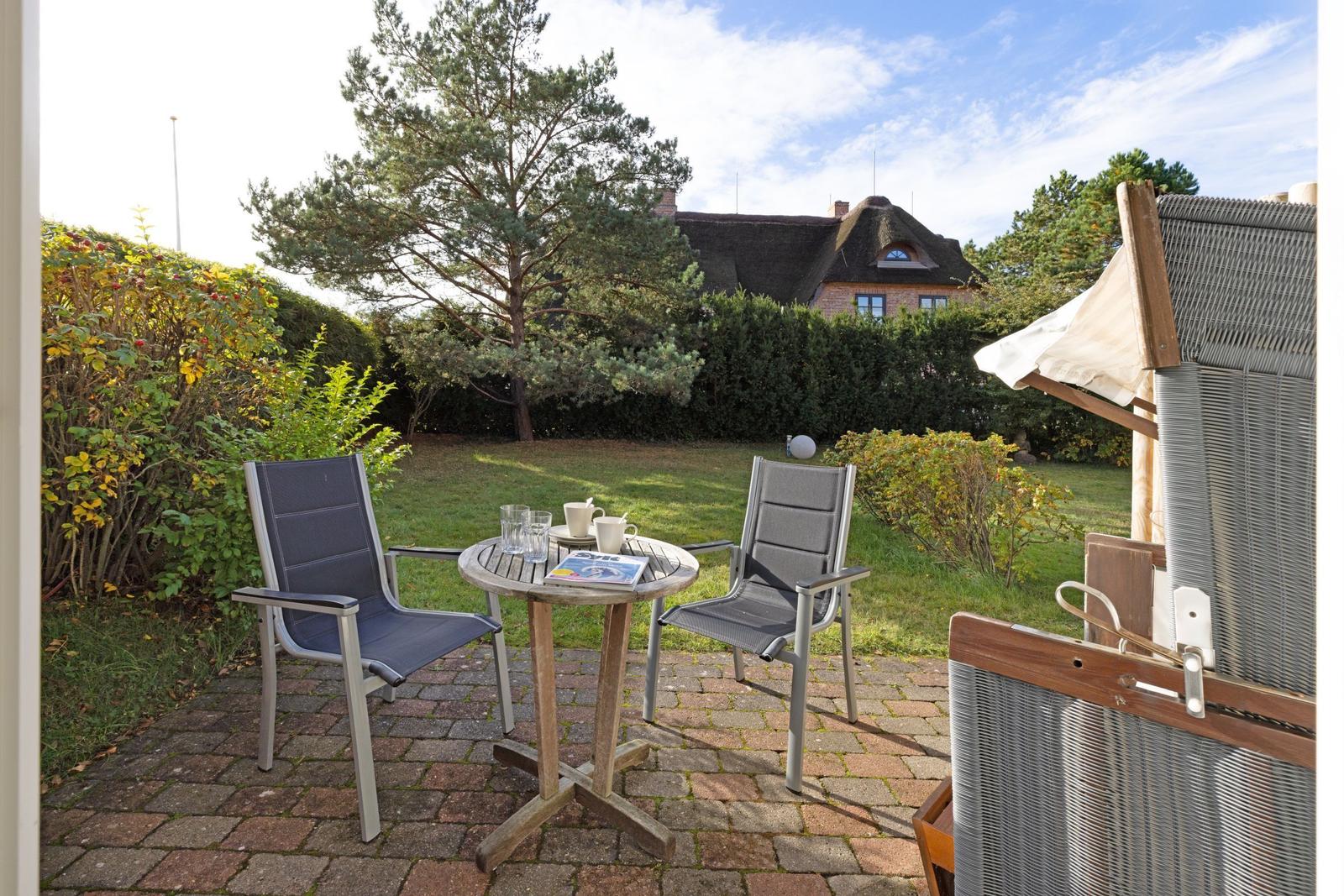 Terrace with table and two chairs. House and trees in the background.