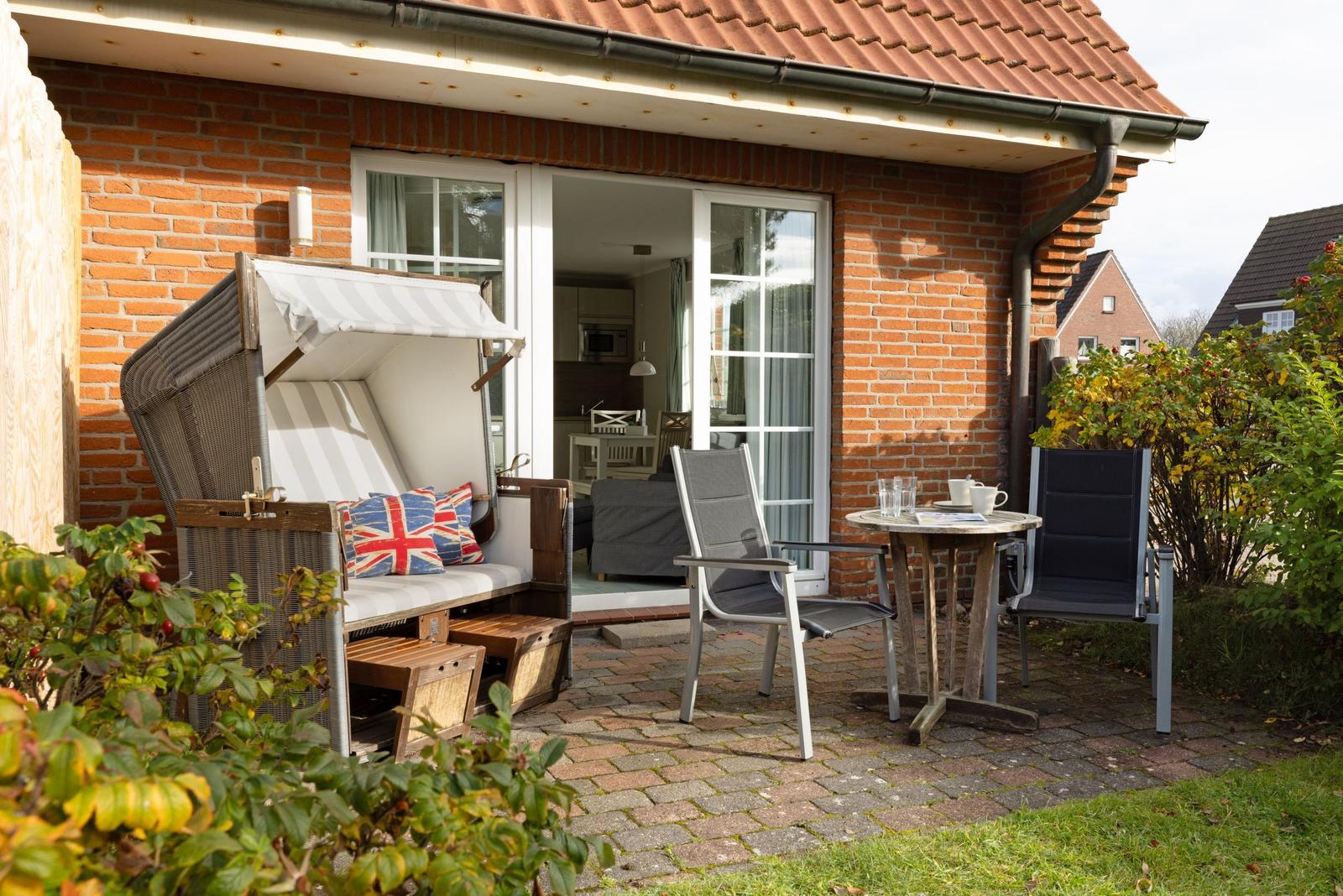 Terrace with lounger, table and chairs in front of a brick house.