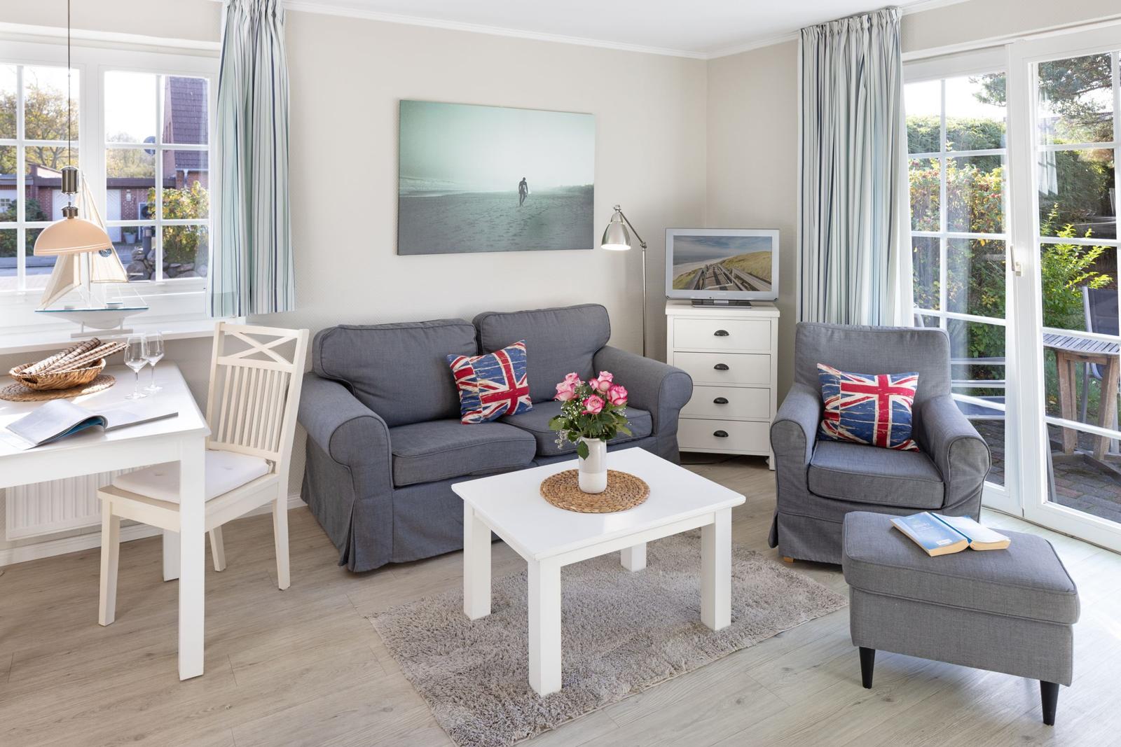 Living room with sofa, armchair, and dining table. Windows with outdoor view.
