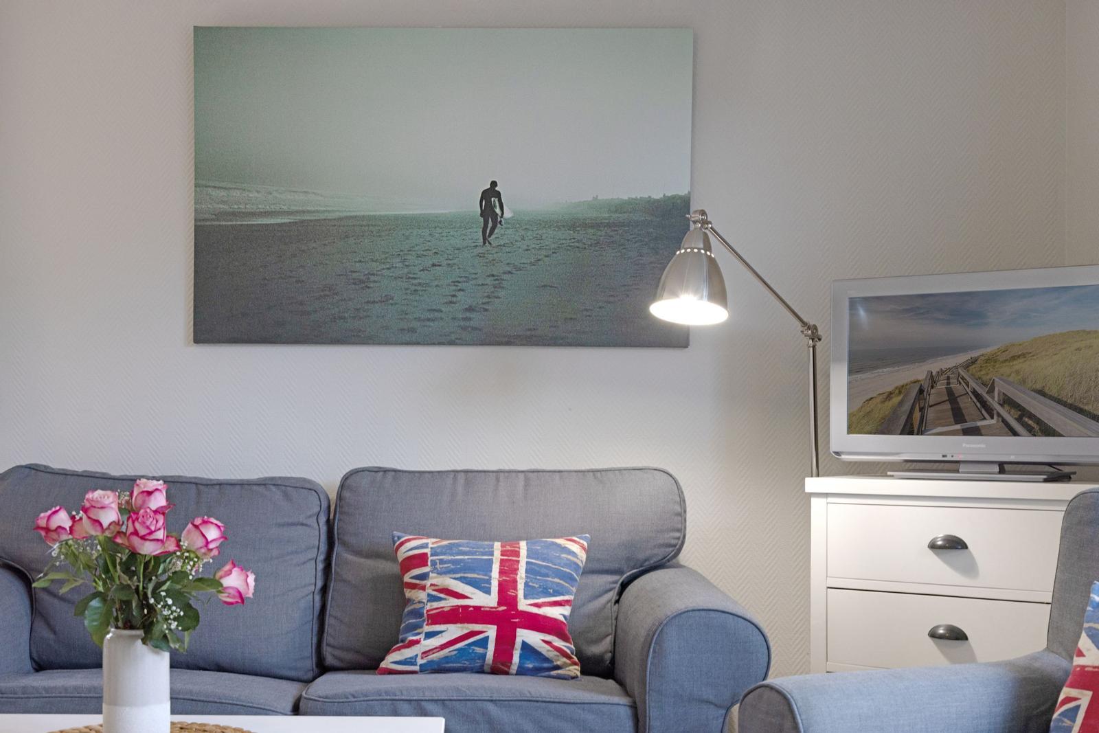A living room with a sofa, flag-patterned cushions, and a wall picture of a surfer.