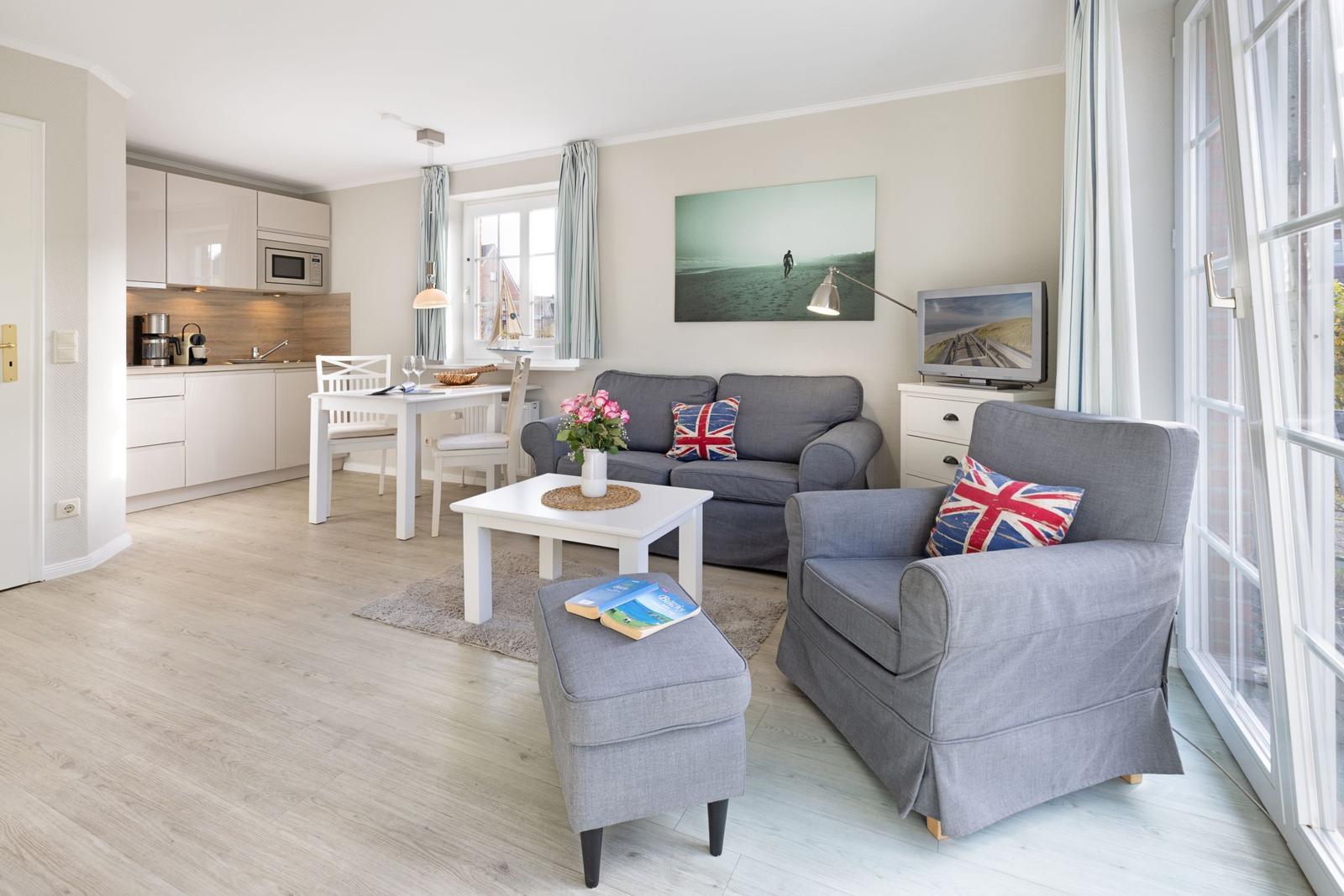 Living and dining area with kitchenette, sofa, and armchair. Windows with view outside.