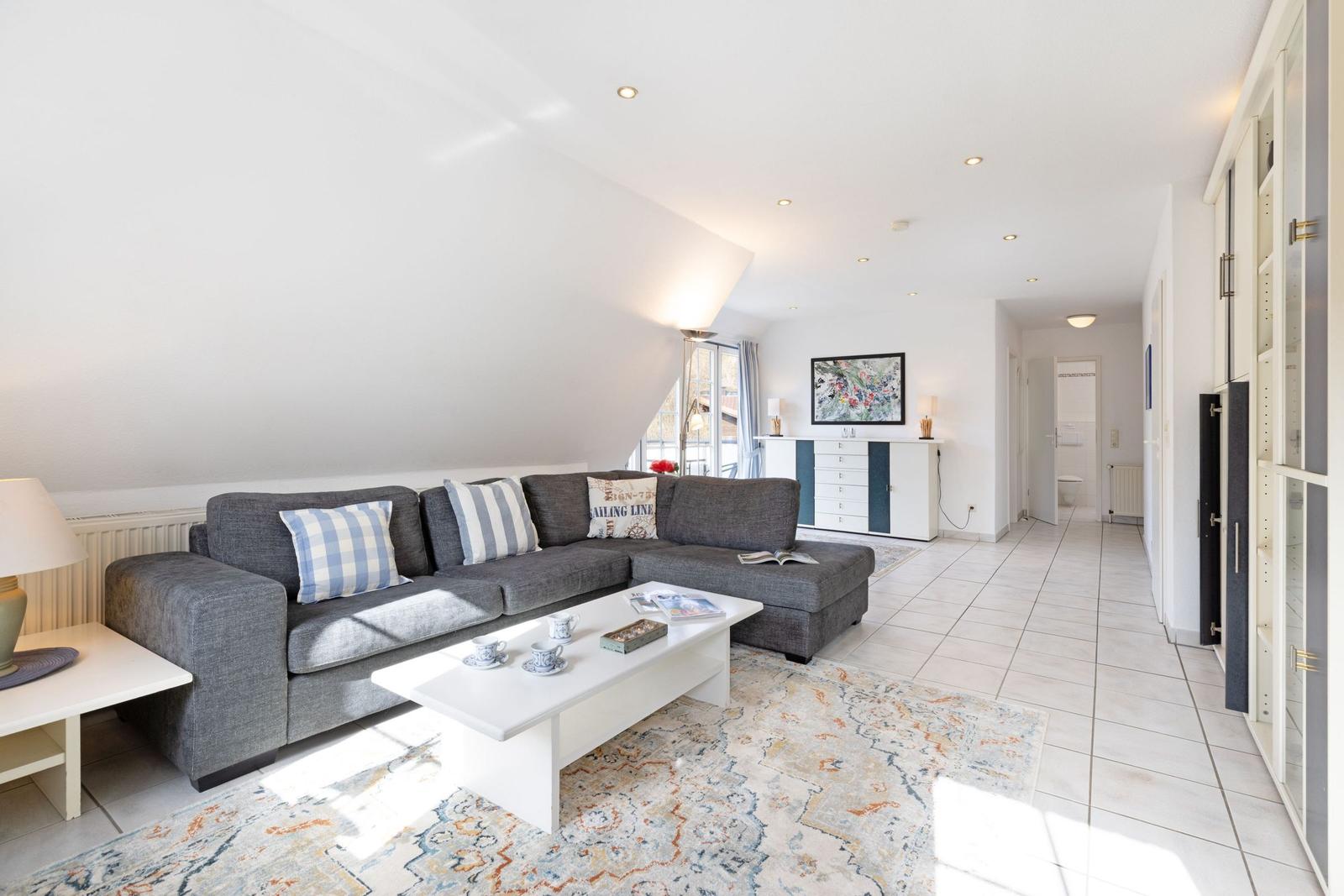 Wohnzimmer mit grauem Sofa, weißem Couchtisch und Teppich auf Fliesenboden.