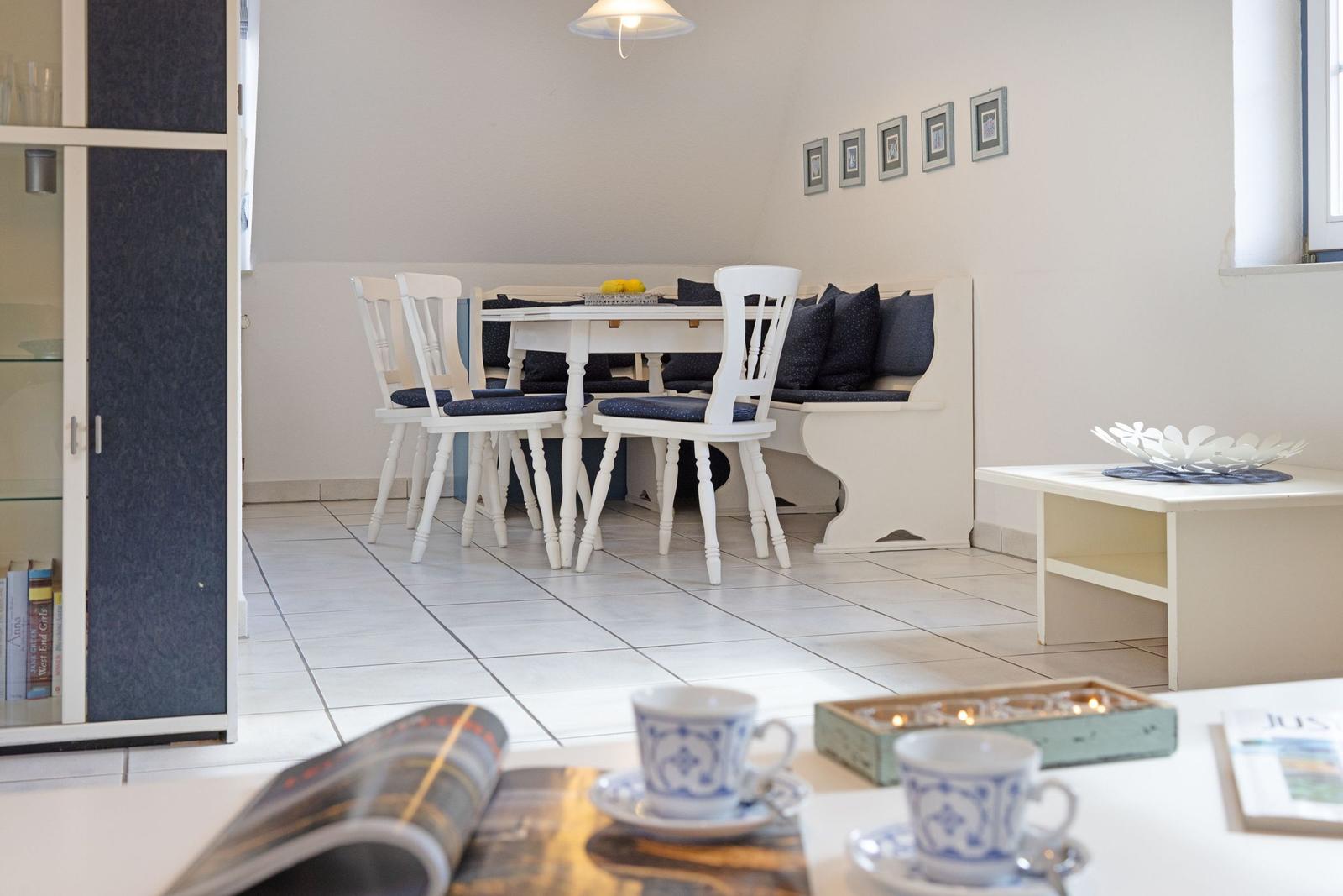 Essbereich mit weißem Tisch, Stühlen und Sitzbank mit Kissen.