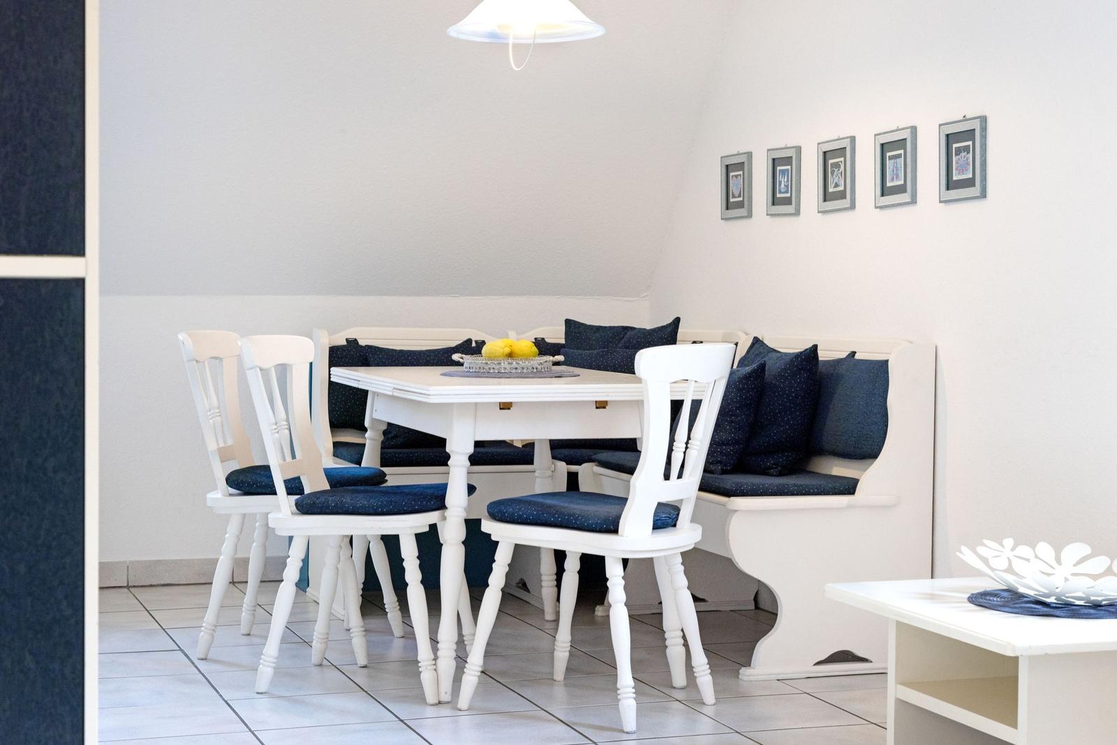 Essbereich mit weißem Tisch, Stühlen und Sitzbank mit blauen Kissen.