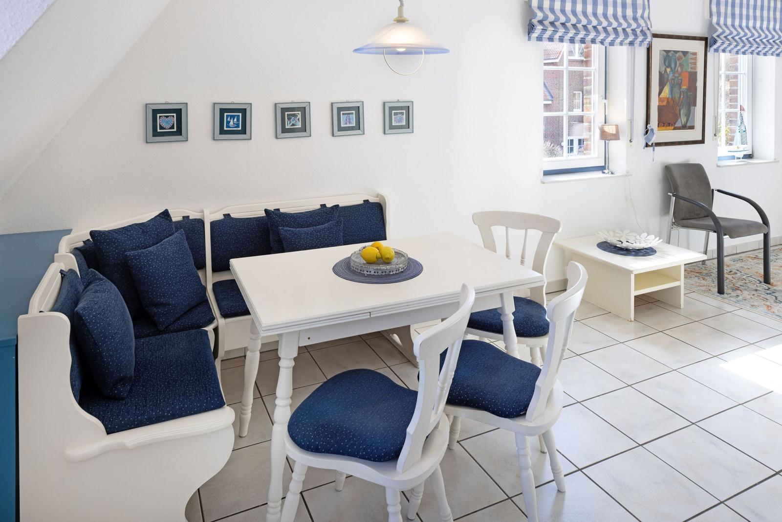 Esszimmer mit weißem Tisch, blauen Kissen und Fenstern mit blau-weißen Rollläden.